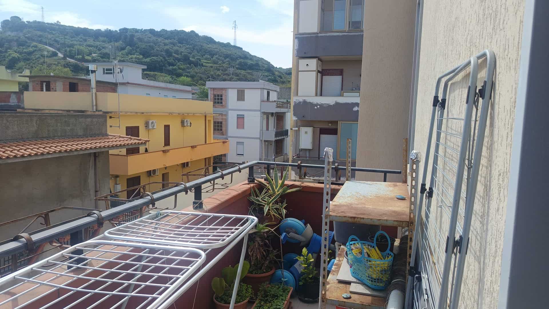 Balcone di un appartamento con piante e decorazioni, vista su edifici e colline circostanti, in un contesto urbano tranquillo, ideale per relax e svago all'aperto.