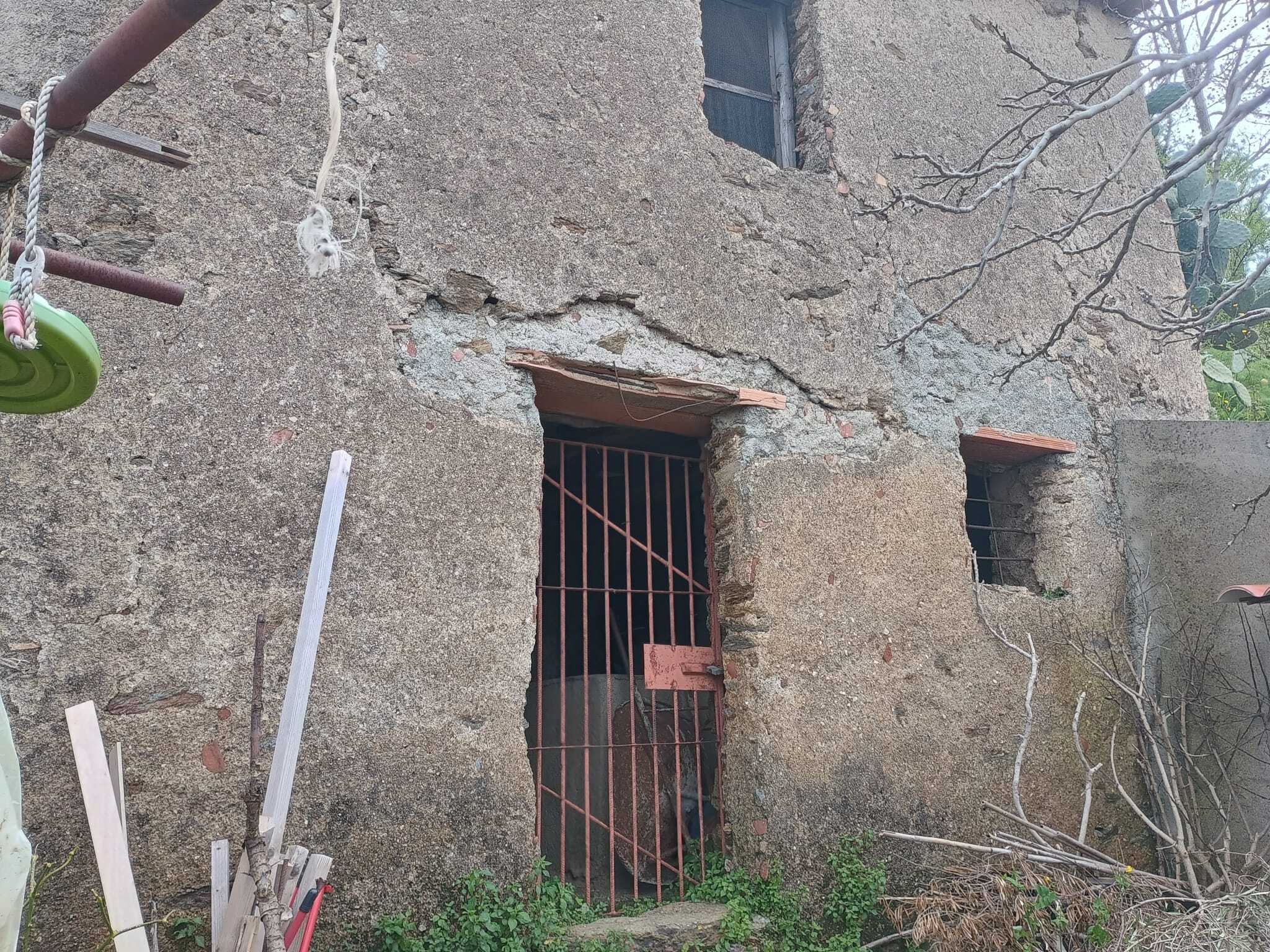 Entrata in muratura con inferriata in ferro, pareti esterne in pietra e ambiente rustico, situata in un contesto naturale.