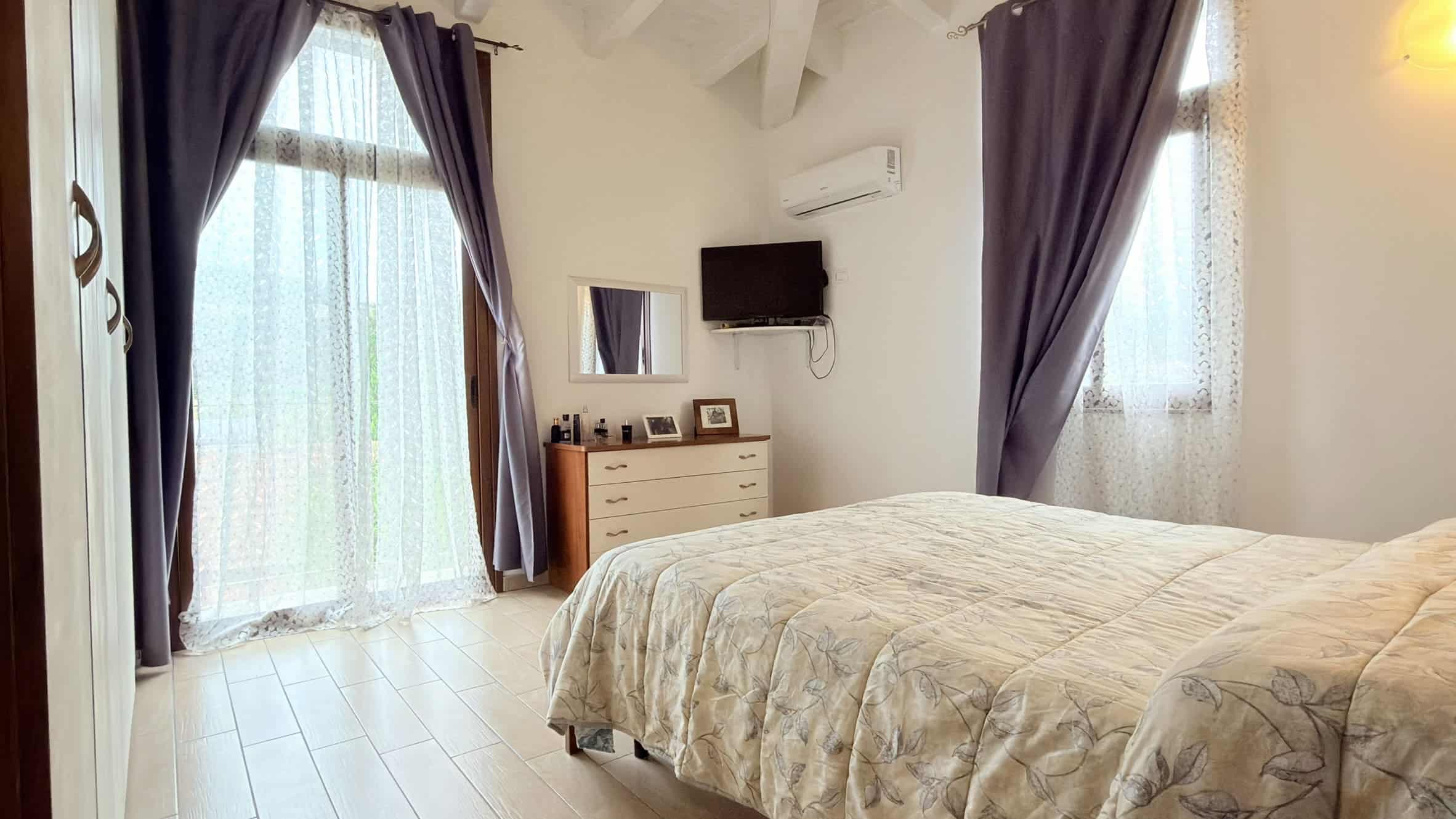 Ampia camera da letto moderna con letto matrimoniale, finestra con tende scure e aria condizionata, arredamento minimalista, ideale per soggiorni confortevoli e rilassanti.