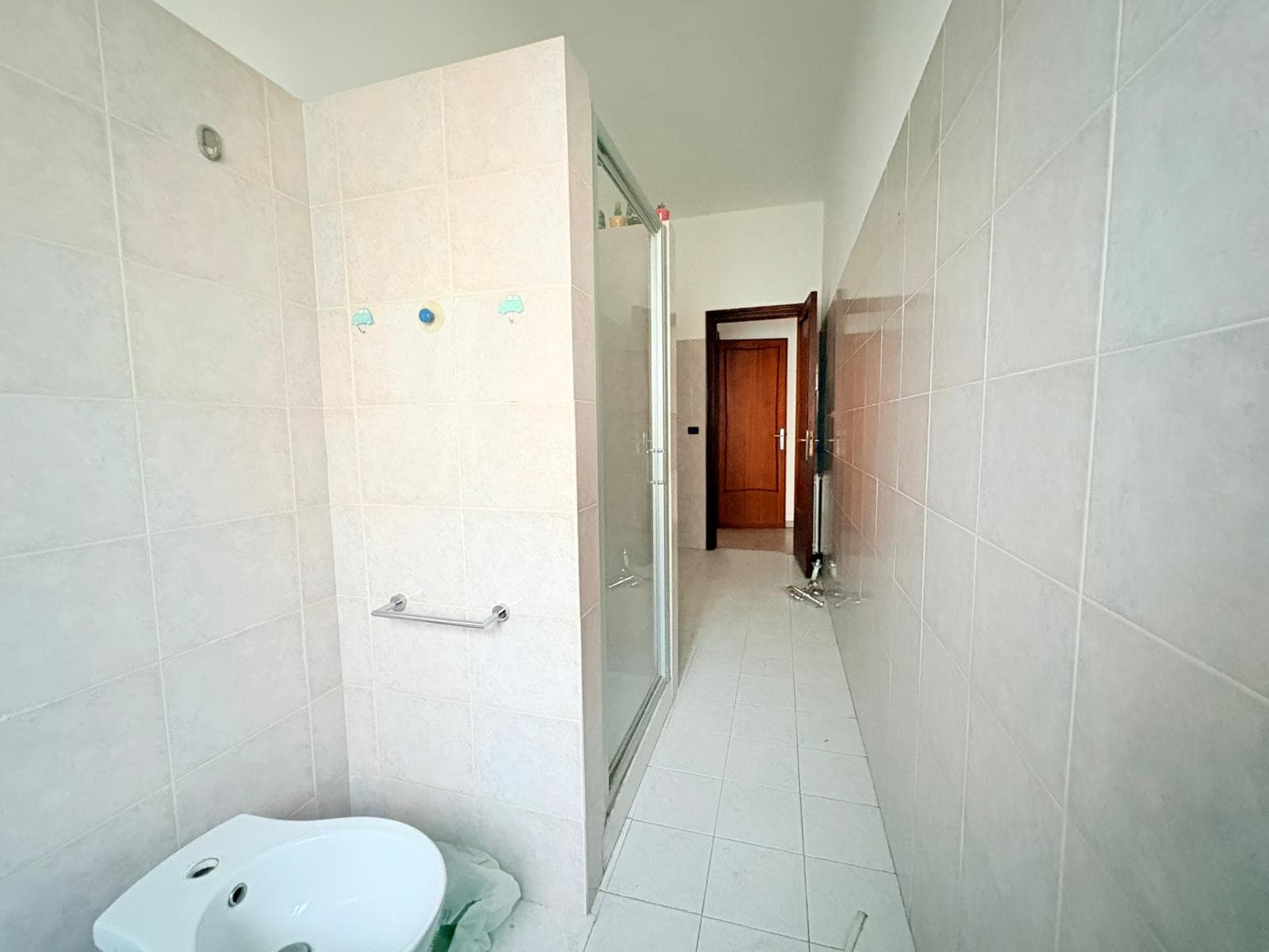 Lavabo e box doccia in un bagno moderno con piastrelle chiare, spazio funzionale e illuminazione naturale, ideale per appartamenti in vendita o affitto.