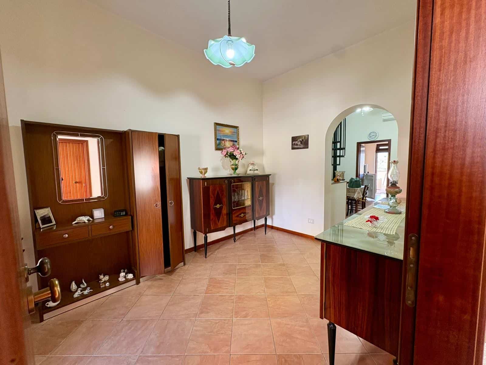 Elegante ingresso di casa con mobili in legno, specchio e decorazioni floreali, illuminato da lampadario a soffitto, in stile classico e accogliente.
