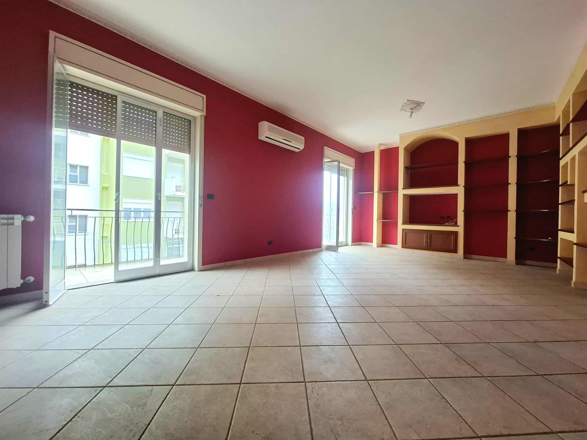 Ampio soggiorno con pareti colorate, balcone e scaffalature in legno, ideale per living e relax, in un appartamento moderno in vendita o affitto a NextCasa.
