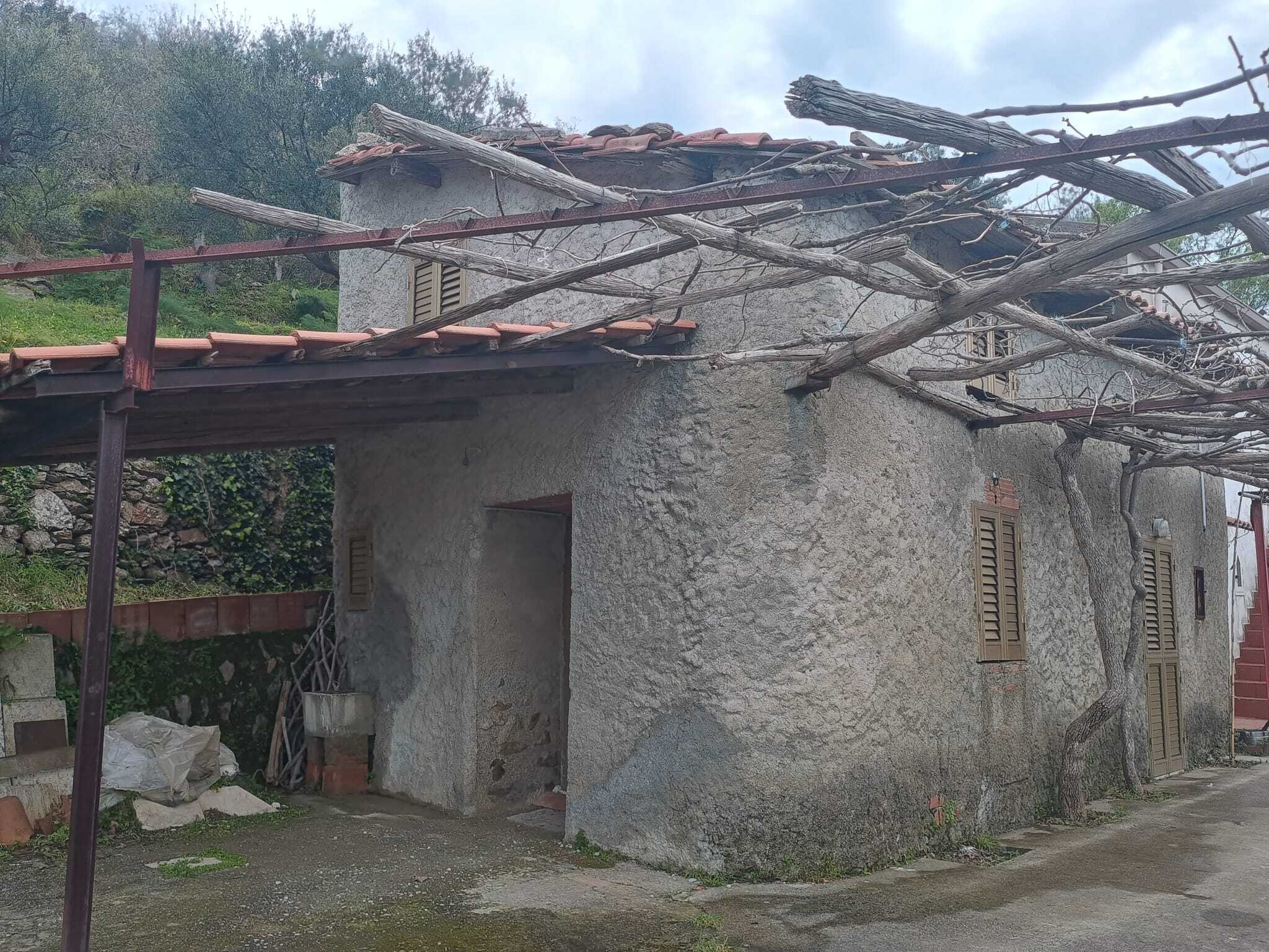 Antico casale in pietra con tetto in tegole rosse, situato in un'area rurale con vegetazione circostante, ideale per ristrutturazione e trasformazione in abitazione o struttura ricettiva.