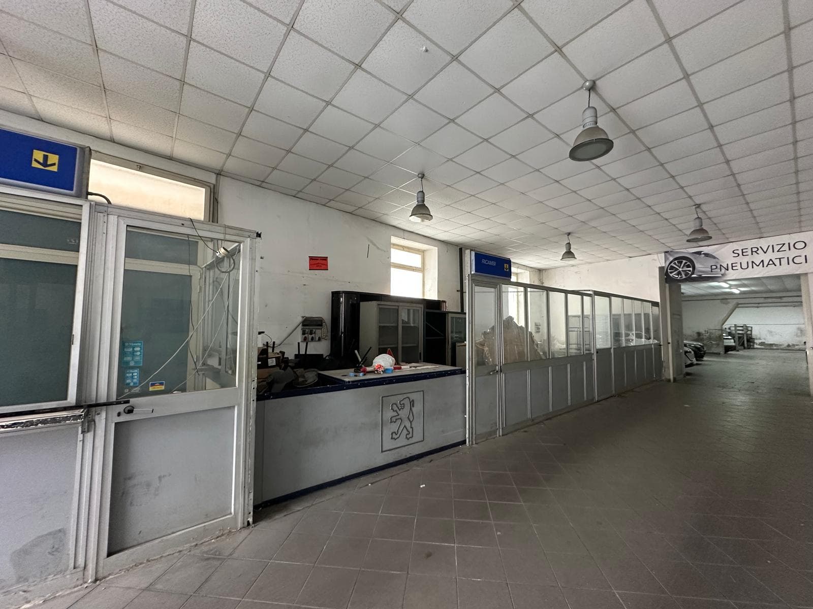 Pannelli di servizio e uffici in un'area di assistenza auto con segnaletica per servizi pneumatici e officina, ambienti spaziosi e ben illuminati, ideali per servizi di manutenzione veicoli e assisten.