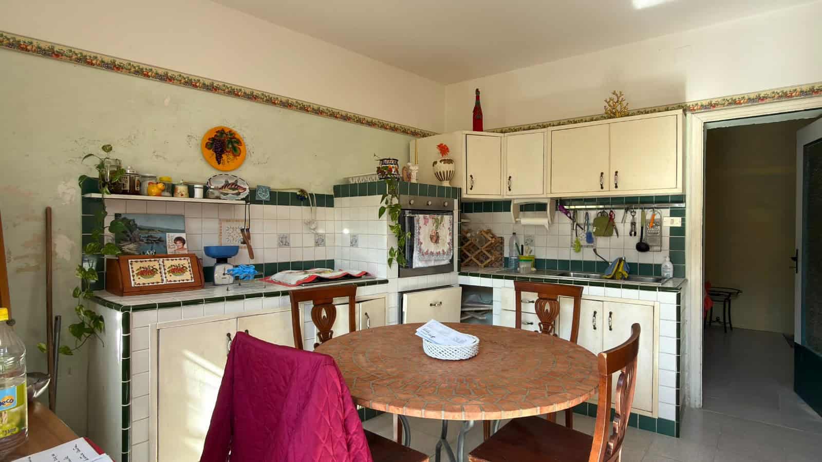 Lavagna di cucina con mobili bianchi, piano di lavoro in pietra, stoviglie e decorazioni, ambiente domestico accogliente e funzionale.