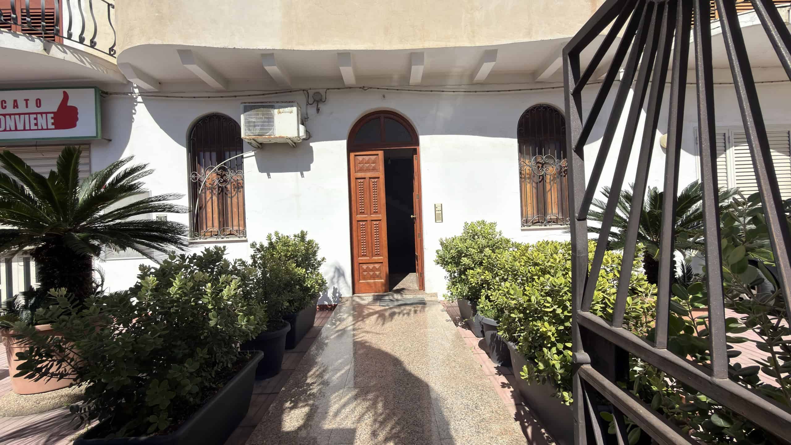 Ingresso di una casa con porta in legno e finestre con grate in ferro, circondato da piante verdi e un'area esterna accogliente, ideale per residenze e affitti turistici.