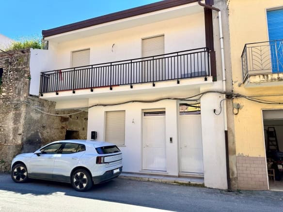 Lavagna di casa moderna con balcone e auto parcheggiata davanti, edificio residenziale in zona urbana.
