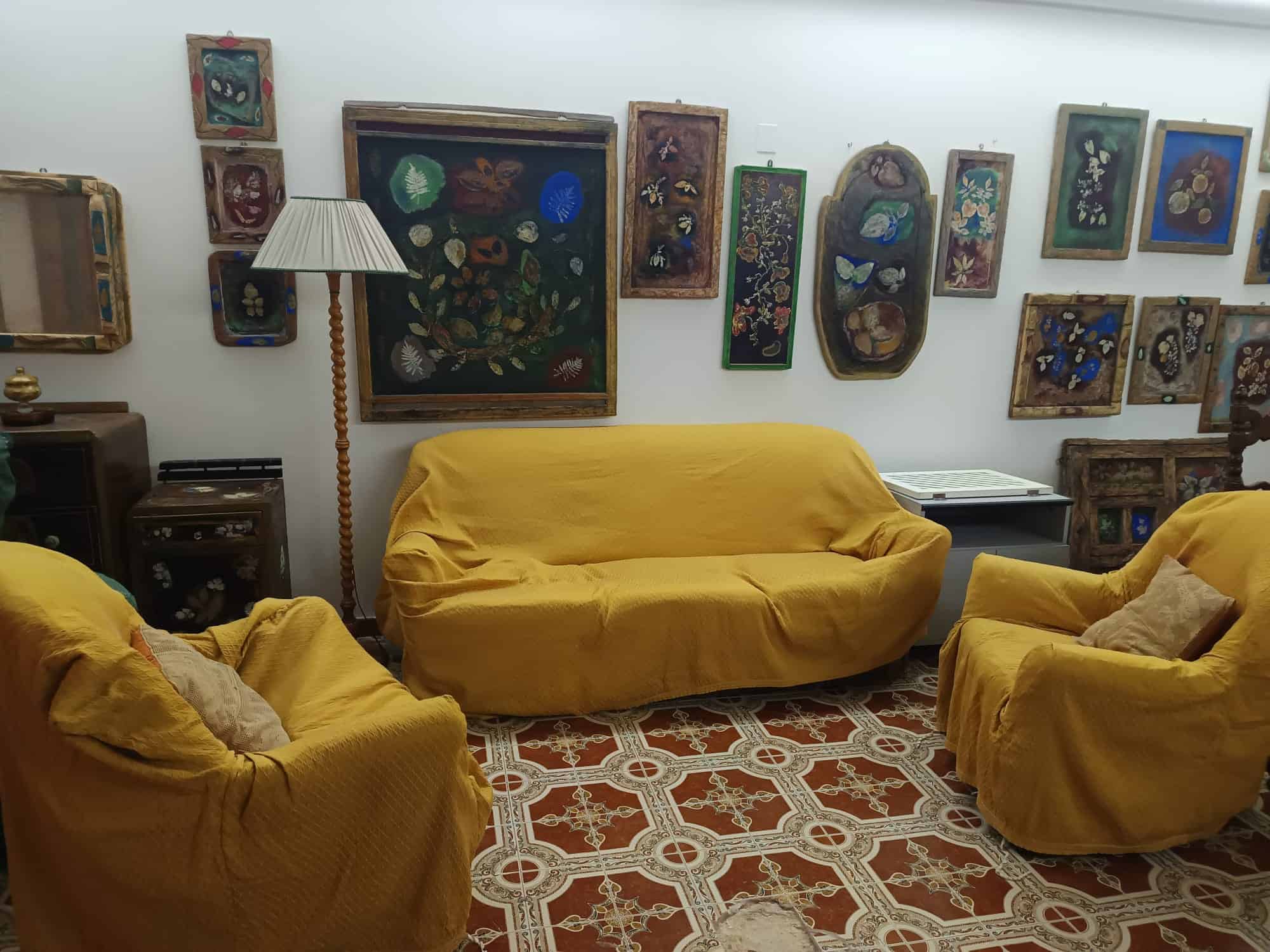 Sedie e divani gialli in un salotto elegante con parete decorata da quadri artistici e un pavimento in piastrelle di design. Perfetto per un ambiente accogliente e di stile.