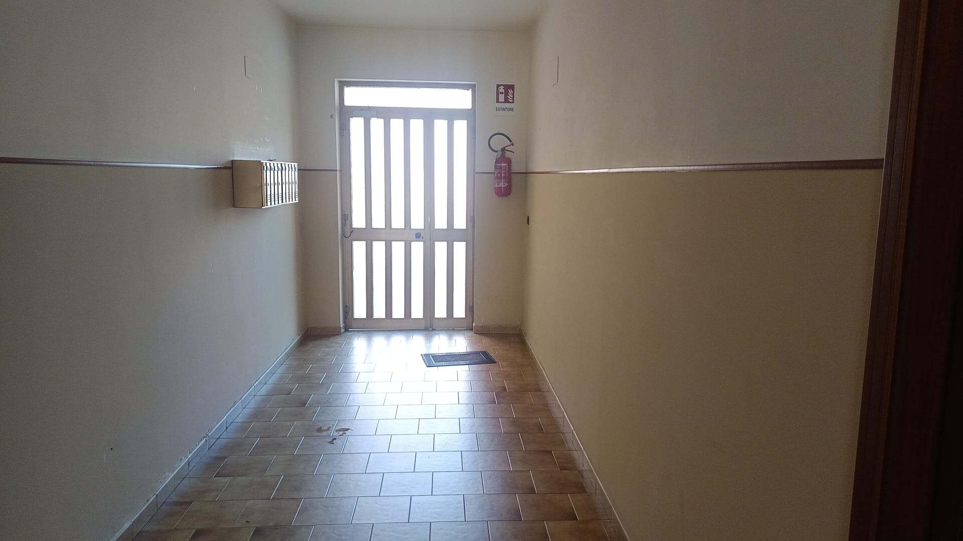 Porta d'ingresso di un appartamento con pavimento in piastrelle e pareti beige, vista dall'interno.
