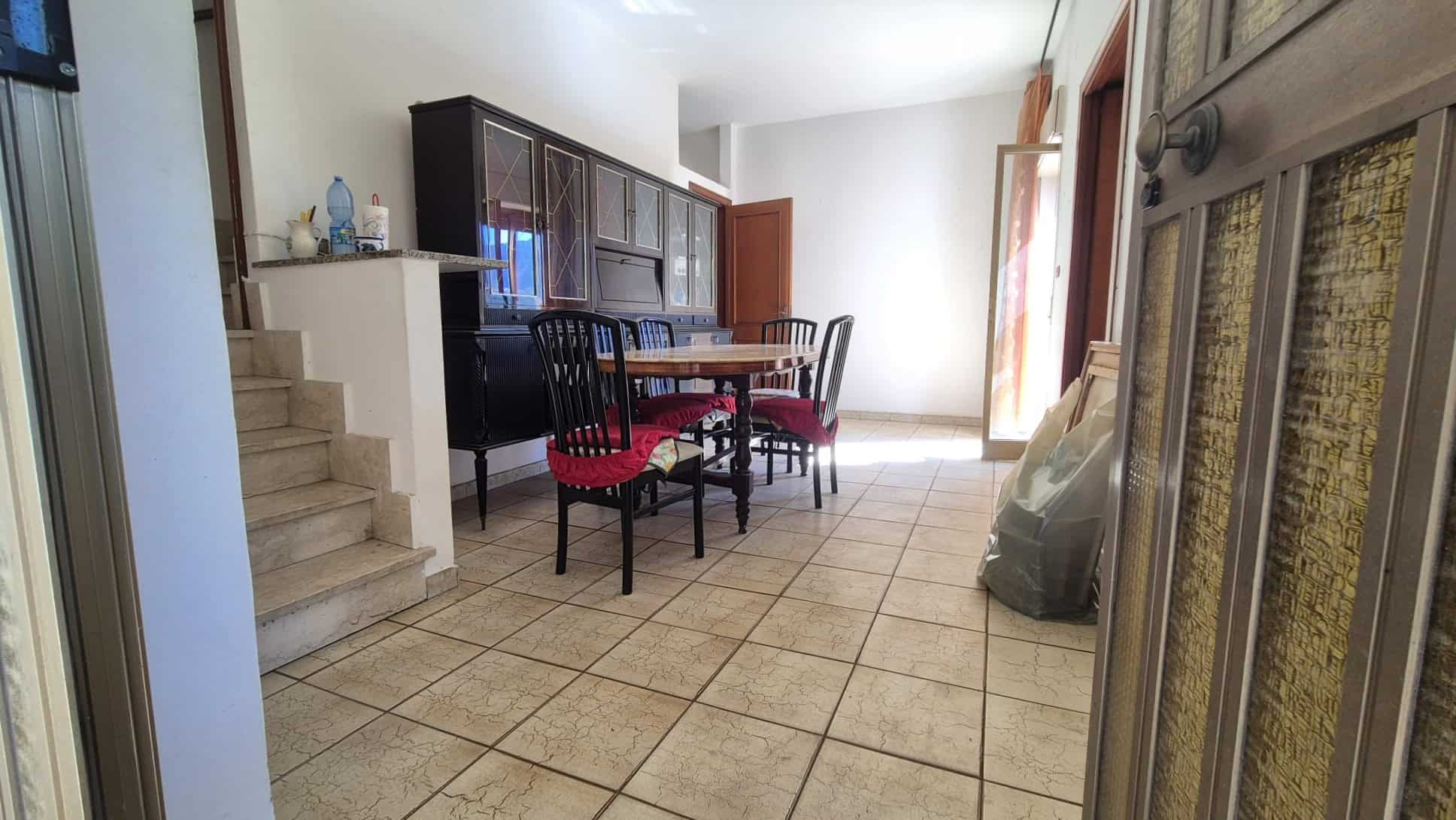 Ampia sala da pranzo con tavolo e sedie in legno, ambiente luminoso e accogliente, ideale per famiglie e incontri conviviali, con accesso a un balcone o terrazza.