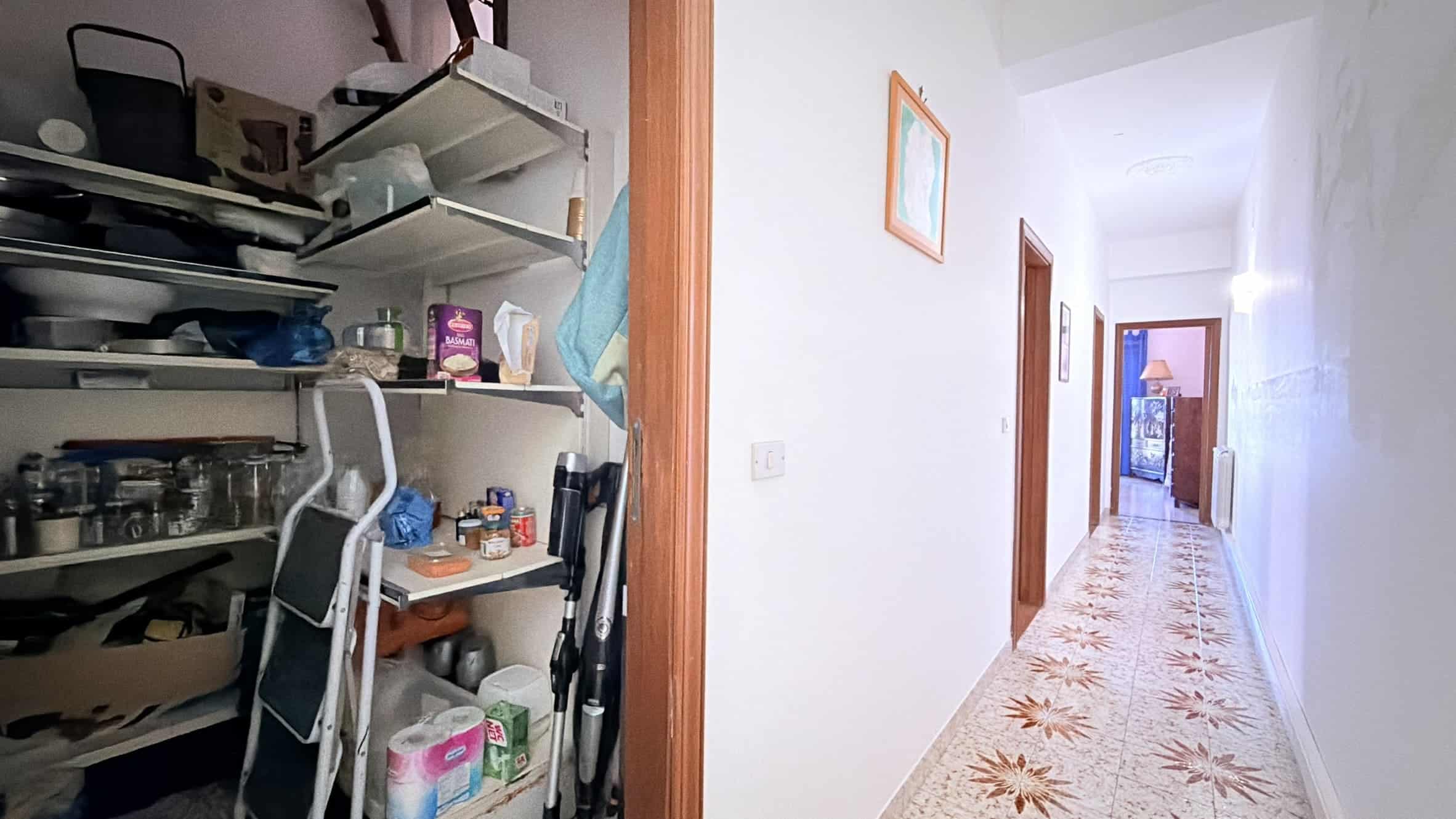 Ripostiglio con scaffali pieni di prodotti e attrezzi, in un corridoio di una casa, ambiente ordinato e funzionale.