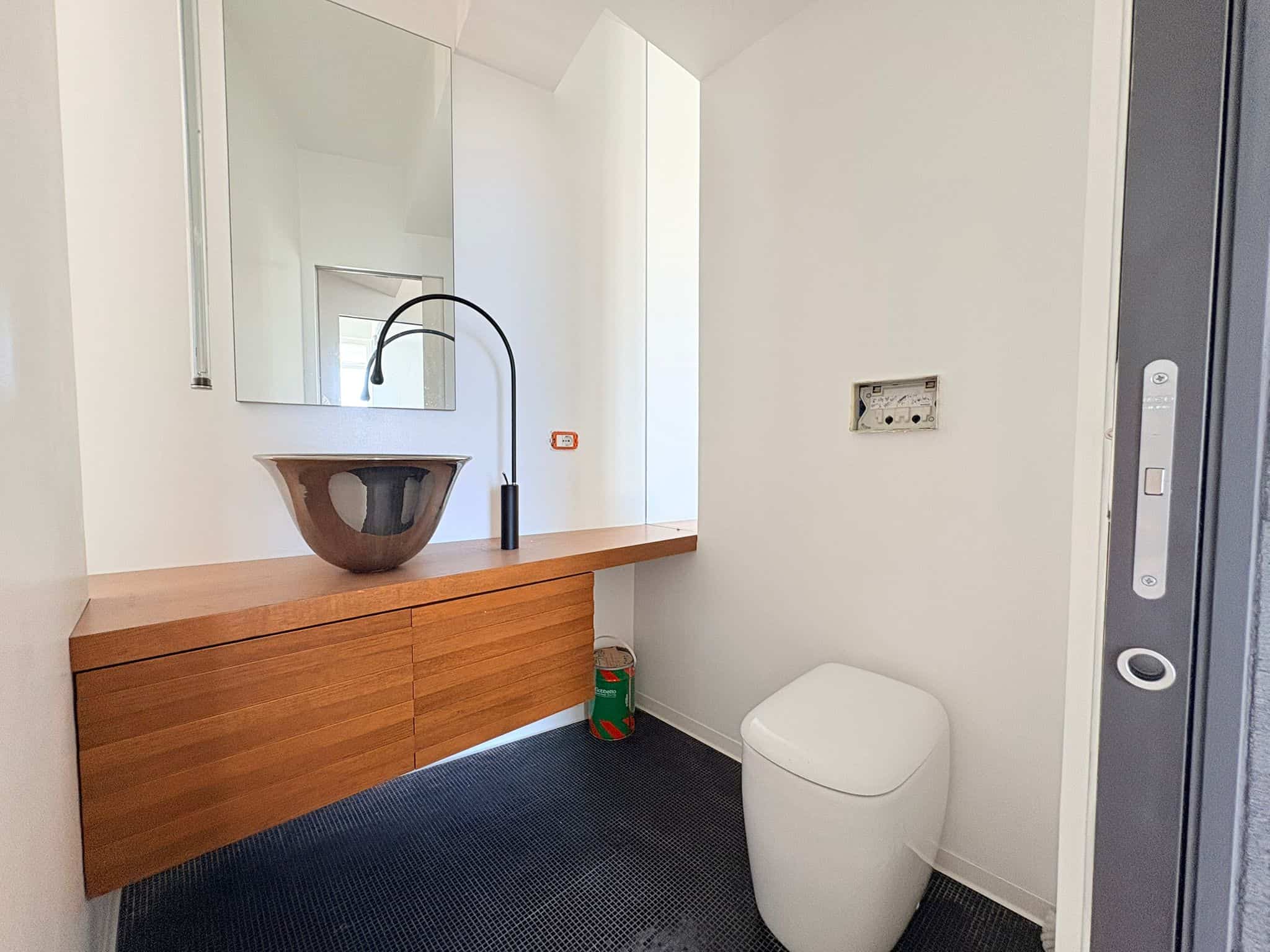 Lavabo sospeso con mobile in legno e rubinetto nero, bagno moderno e minimalista, pareti bianche e pavimento scuro, spazio funzionale e elegante, ideale per abitazioni di design.