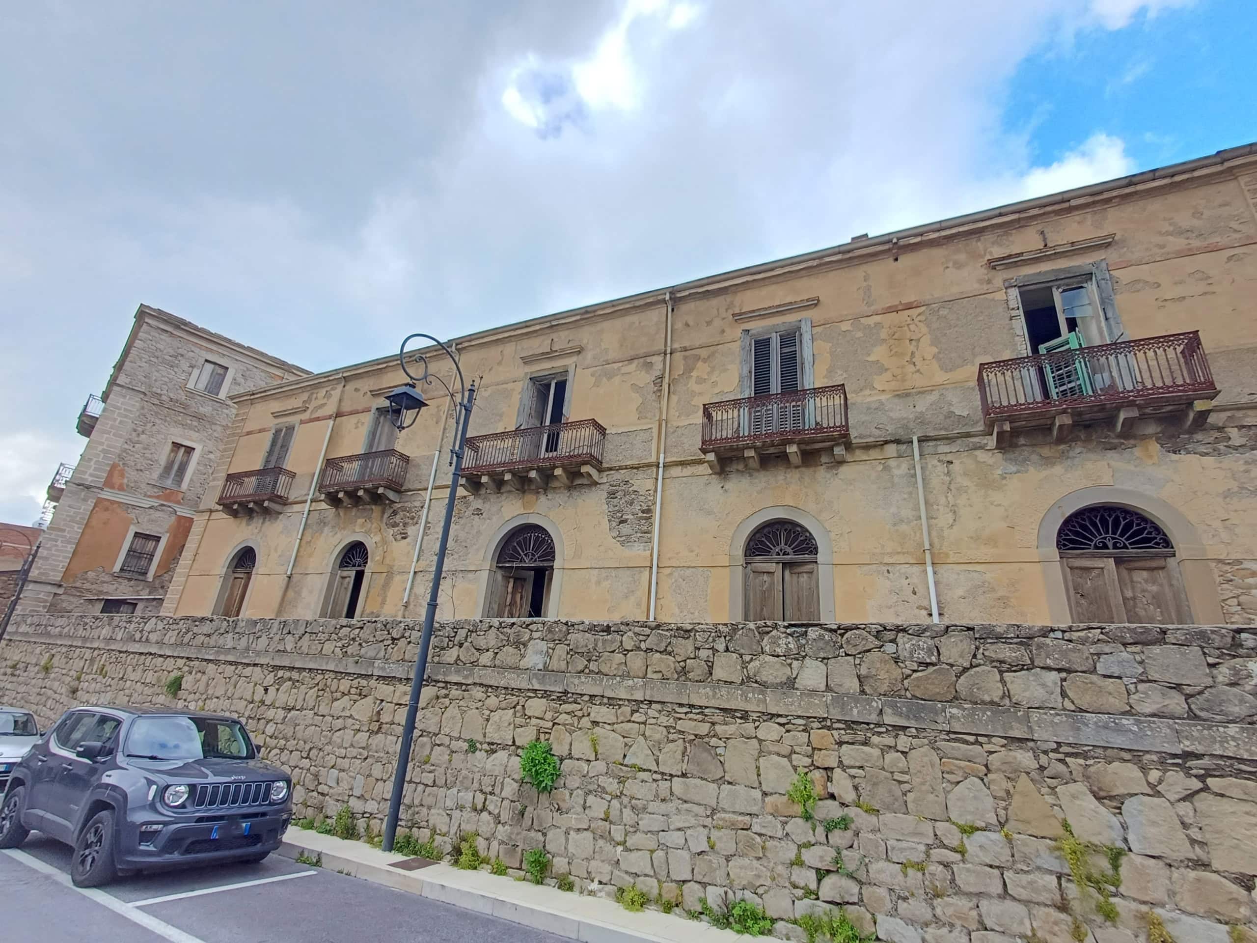 Villa storica in pietra con balconi in legno, situata in un quartiere storico, con parcheggio e vista panoramica sulla città. Perfetta per investimenti immobiliari o residenze di charme in Italia.