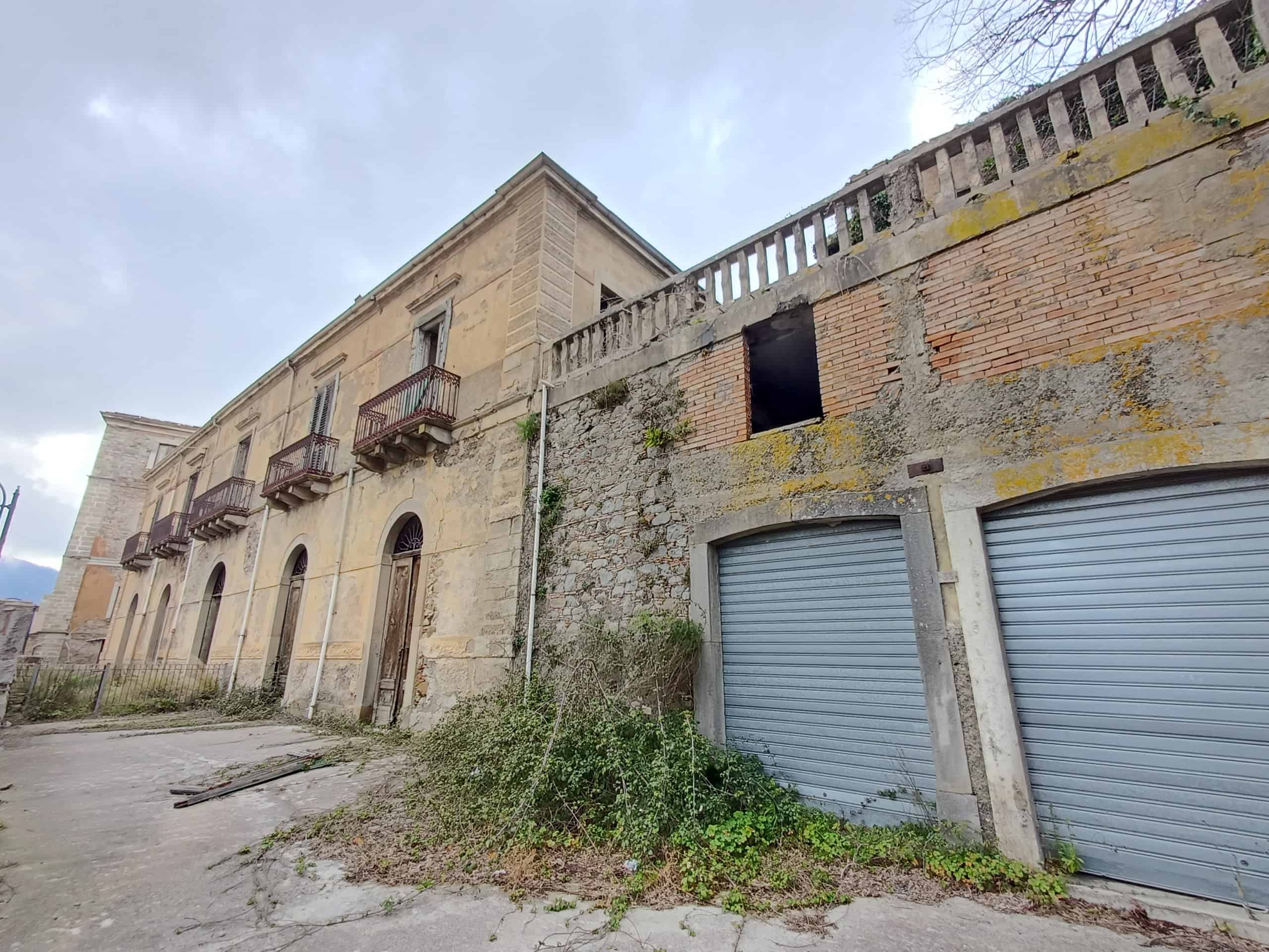 Vicolo con edifici storici in pietra e garage con serrande metalliche, atmosfera urbana e rurale, dettagli architettonici, facciata antica, ambiente di strada, Italia, NextCasa.