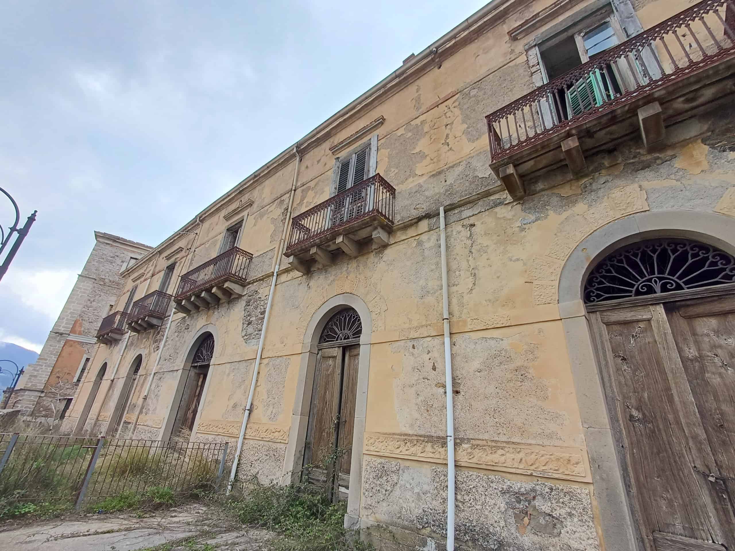 Balcone in legno e facciata di un edificio storico in stile italiano, con pareti in pietra e dettagli architettonici tradizionali.