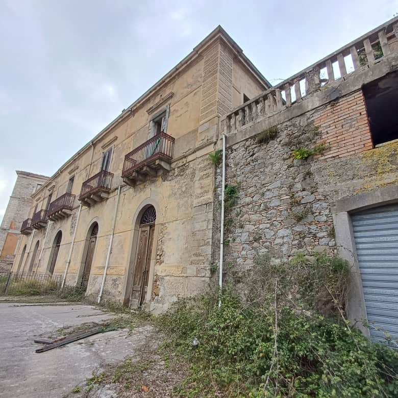Edificio storico in pietra con balconi in ferro battuto e garage, situato in una zona collinare con vista panoramica, in stile classico italiano.