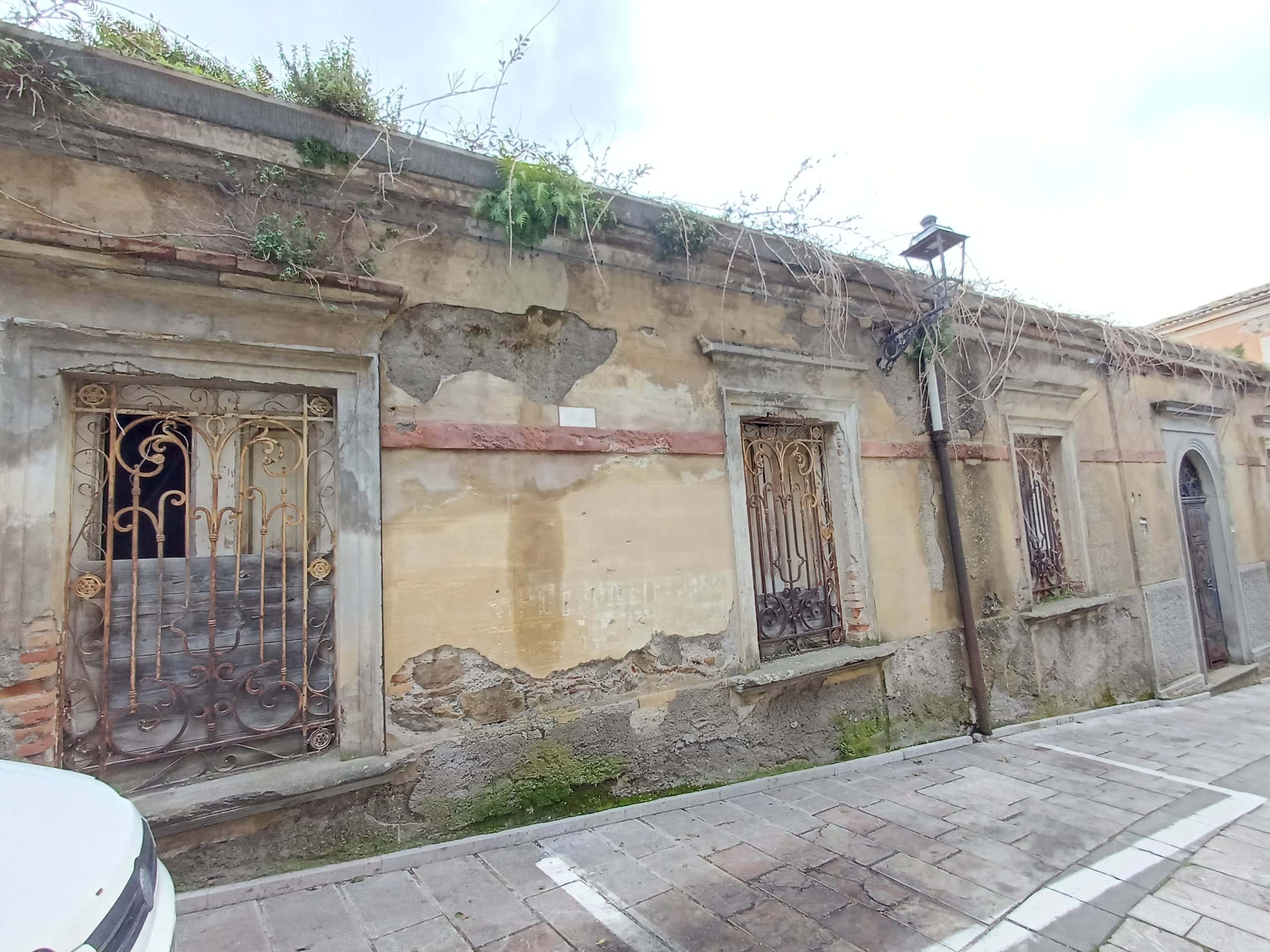Vetri antichi e pareti in pietra di un edificio storico, con inferriate decorative alle finestre, in un contesto urbano.