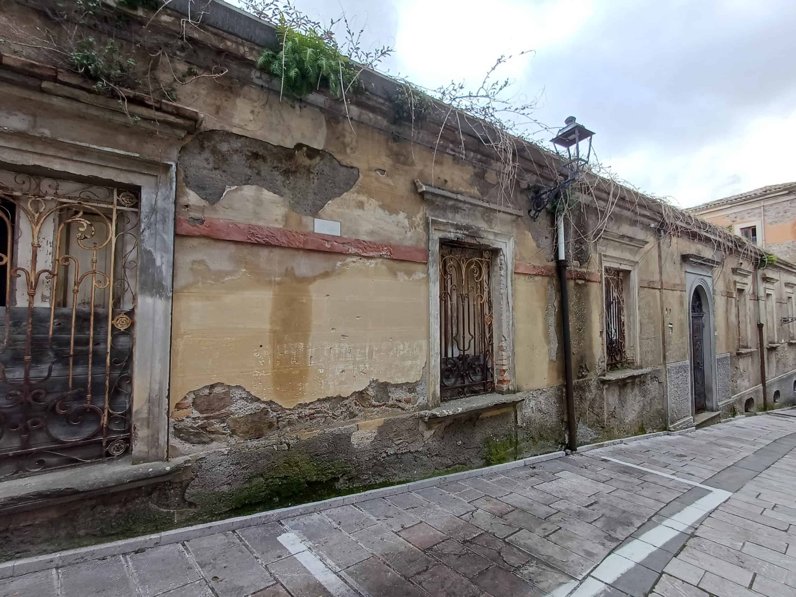 Finestra antica con grate in ferro battuto su parete di un edificio storico, strada pavimentata in pietra, atmosfera urbana e suggestiva.