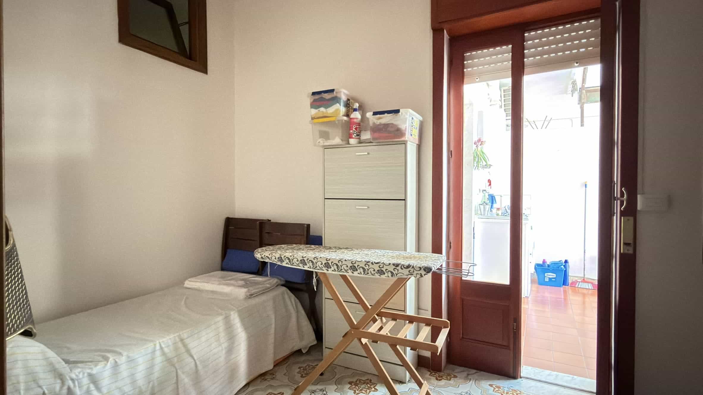 Letto singolo in camera con accesso a balcone, arredamento semplice e luce naturale, ideale per ambienti di soggiorno o studio.