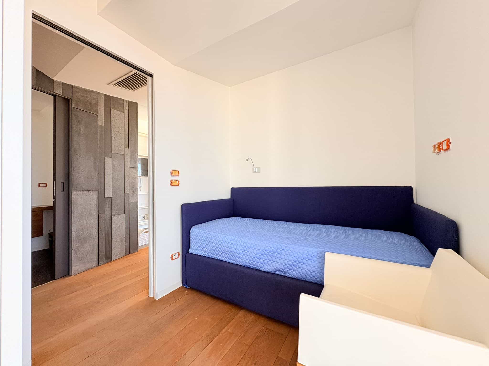 Una stanza moderna con divano letto blu e pareti bianche, ideale per soggiorni confortevoli e funzionali in appartamenti di design. Perfetta per affitti a breve termine o residenze di qualità.