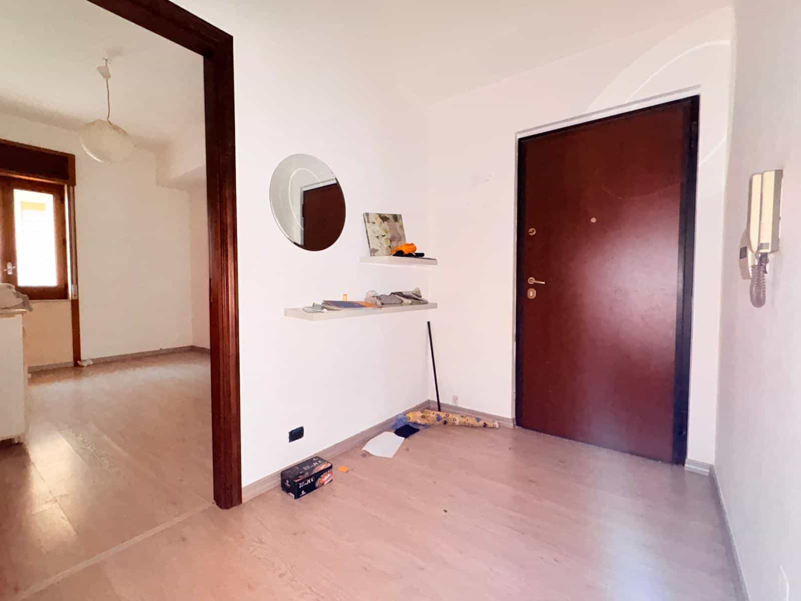 Porte d'ingresso moderna in un appartamento luminoso con pareti bianche e pavimento in legno chiaro, ingresso accogliente con specchio rotondo e mensole decorative.