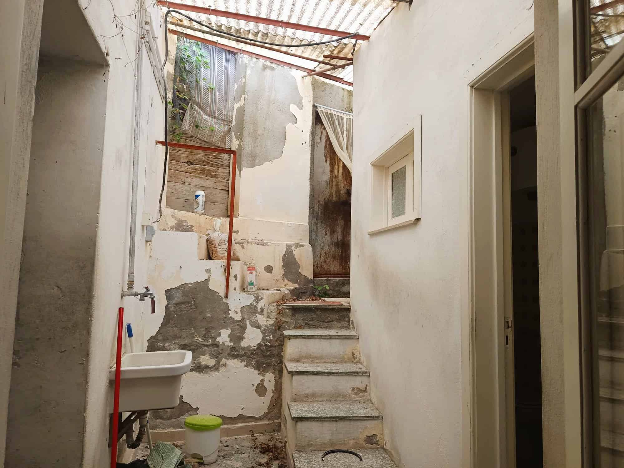 Porte di accesso a un cortile interno con scale in pietra e pareti in cattivo stato di manutenzione, con elementi di ristrutturazione in corso e un lucernario in vetro.