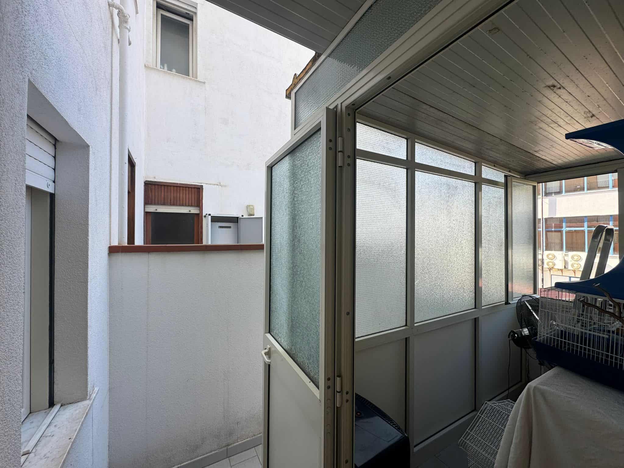 Balcone con veranda in alluminio e vetro, spazio esterno coperto e protetto, ideale per relax e attività all'aperto, in un contesto residenziale moderno e luminoso.