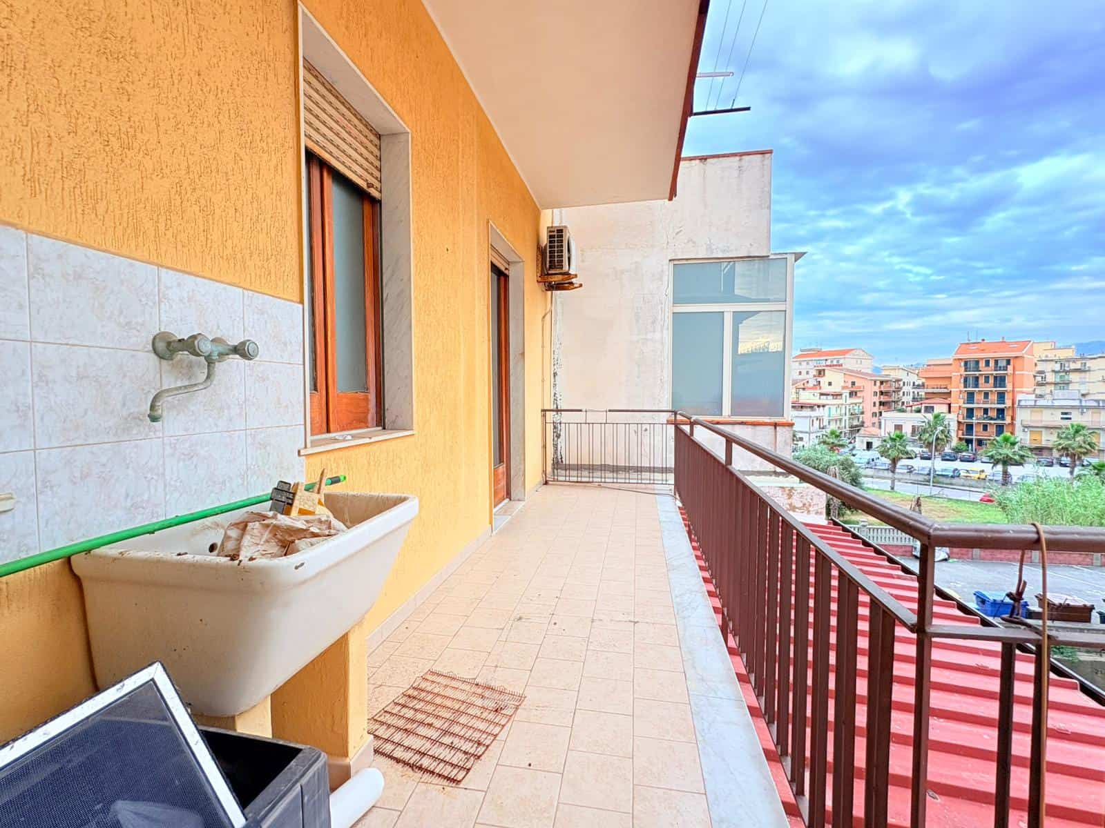 Balcone di un appartamento con vista sulla città, con ringhiera in metallo e pavimentazione in piastrelle, in un complesso residenziale moderno e ben mantenuto.