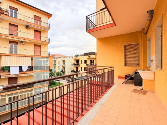 Balcone di un appartamento in un complesso residenziale urbano, con vista su edifici circostanti, pavimentazione in piastrelle e arredi da esterno, ideale per relax e socializzazione.