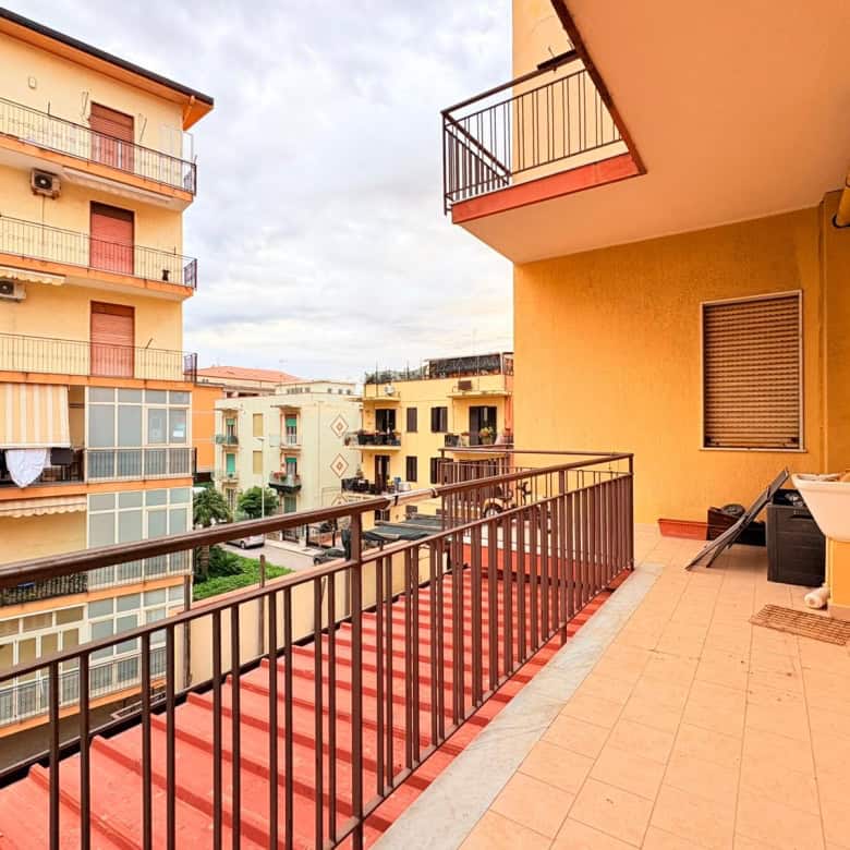 Balcone di un appartamento in un complesso residenziale urbano, con vista su edifici circostanti, pavimentazione in piastrelle e arredi da esterno, ideale per relax e socializzazione.