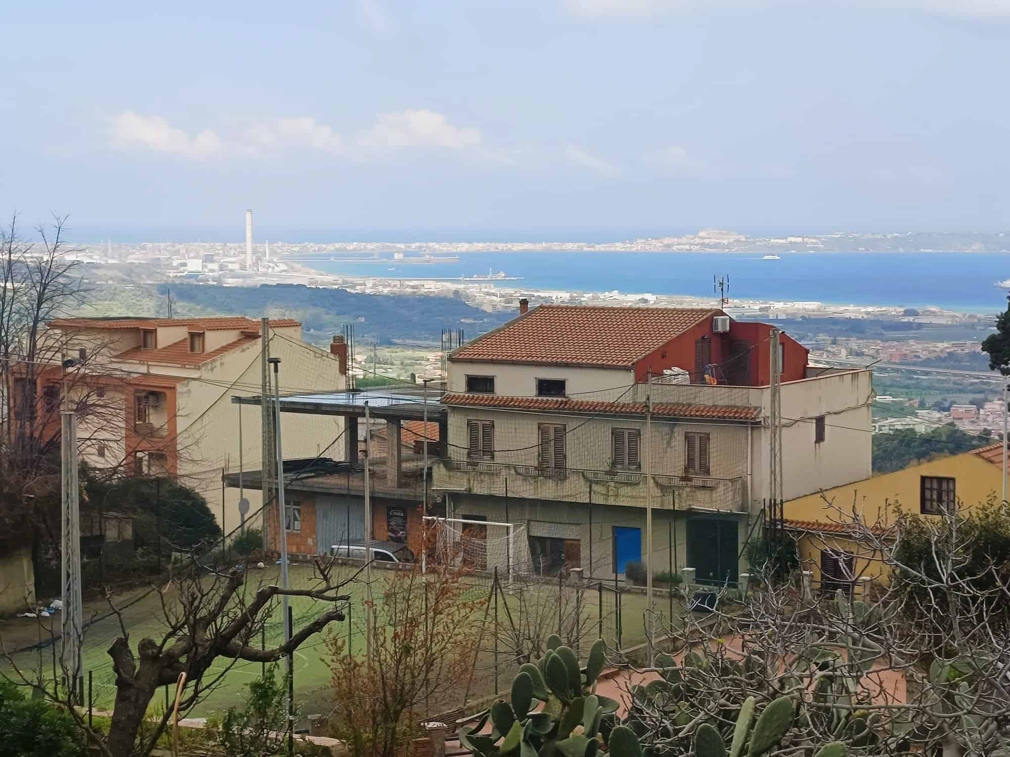 Vista panoramica di case e natura con vista sul mare e sulla città, in zona collinare, con edifici residenziali e vegetazione, in Italia.
