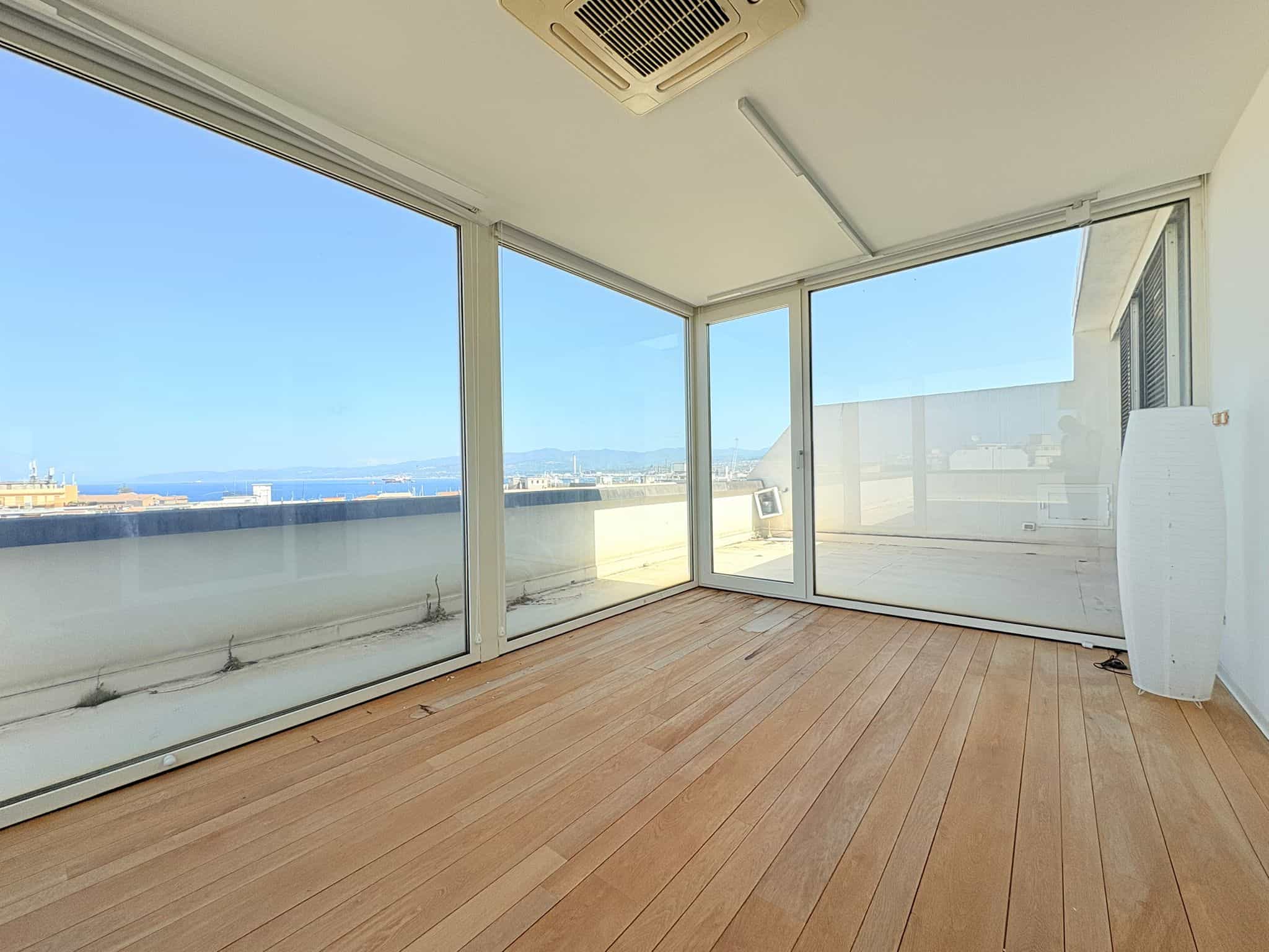 Balcone con ampie vetrate e vista mare, pavimento in legno, ambiente luminoso e moderno, ideale per relax e convivialità.