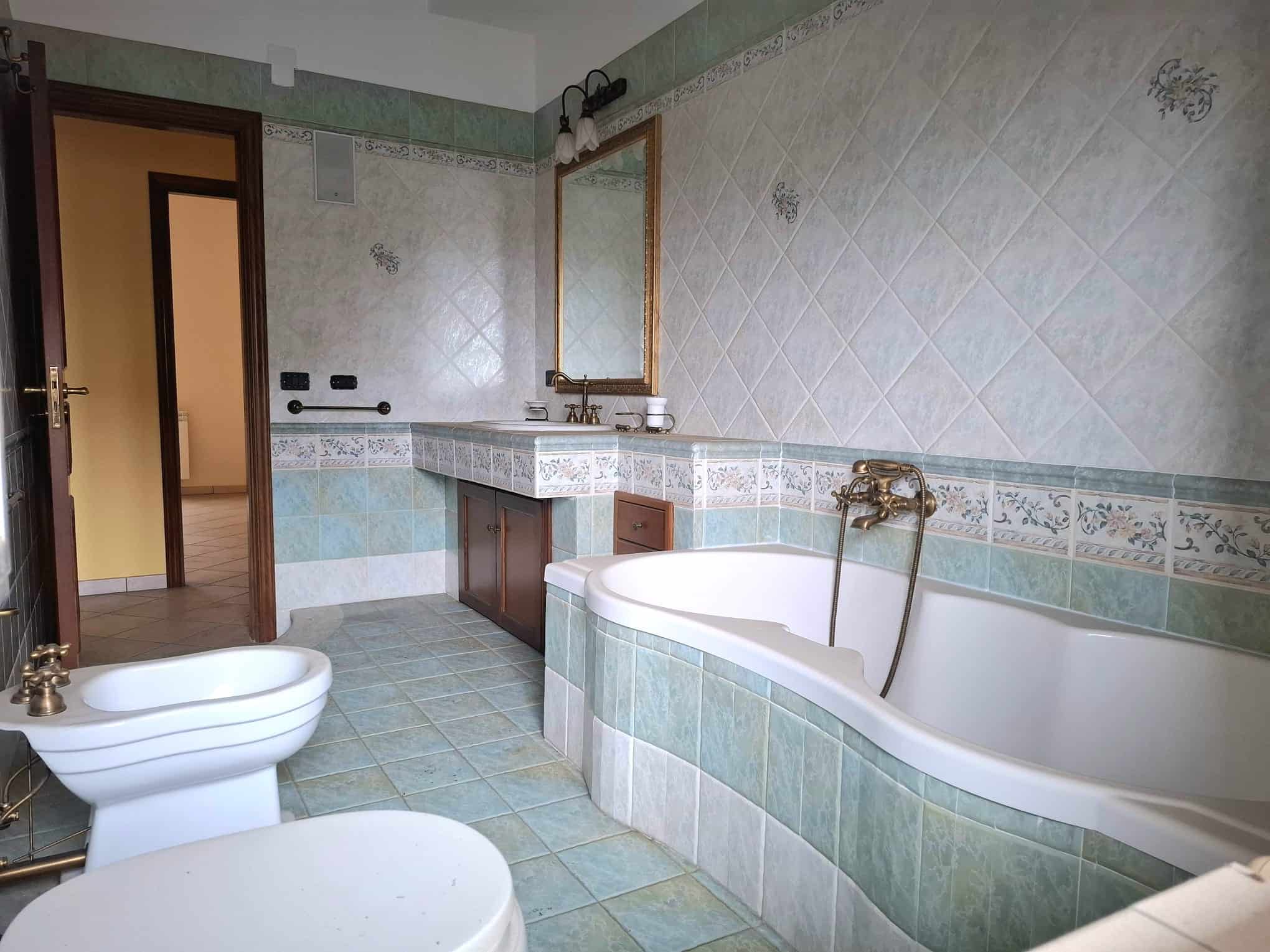 Lavabo e vasca da bagno in un bagno elegante con piastrelle decorative e specchio grande, ambiente luminoso e accogliente, ideale per il comfort e il relax domestico.