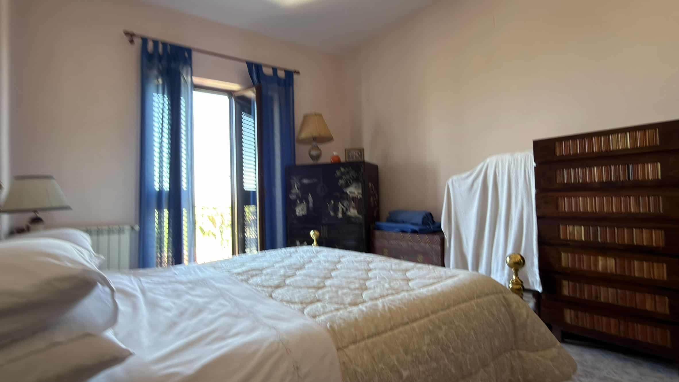 Letto matrimoniale in camera da letto con finestra e tende blu, arredi classici e atmosfera accogliente, ideale per soggiorni confortevoli e rilassanti.