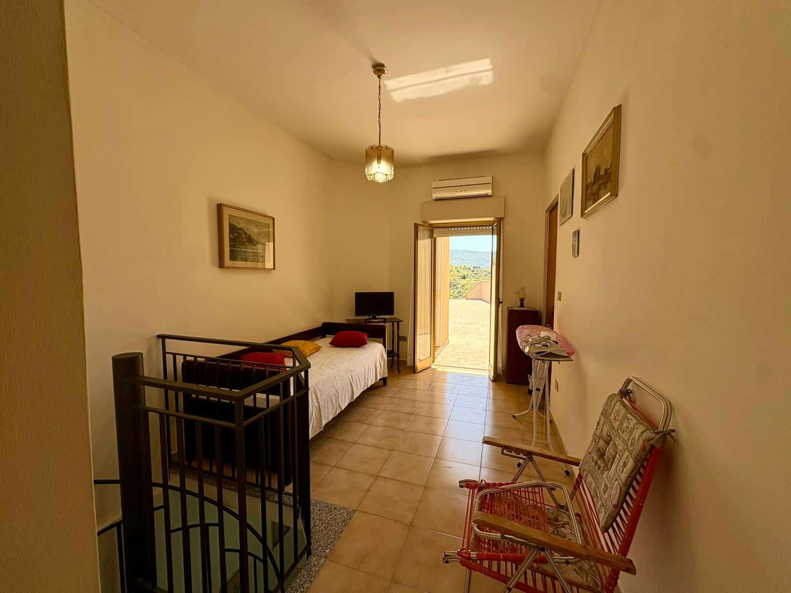 Letto singolo in camera con vista su balcone, arredamento semplice e funzionale, ideale per affitti brevi o soggiorni di relax. Ambientazione luminosa e accogliente, perfetta per un soggiorno conforte.