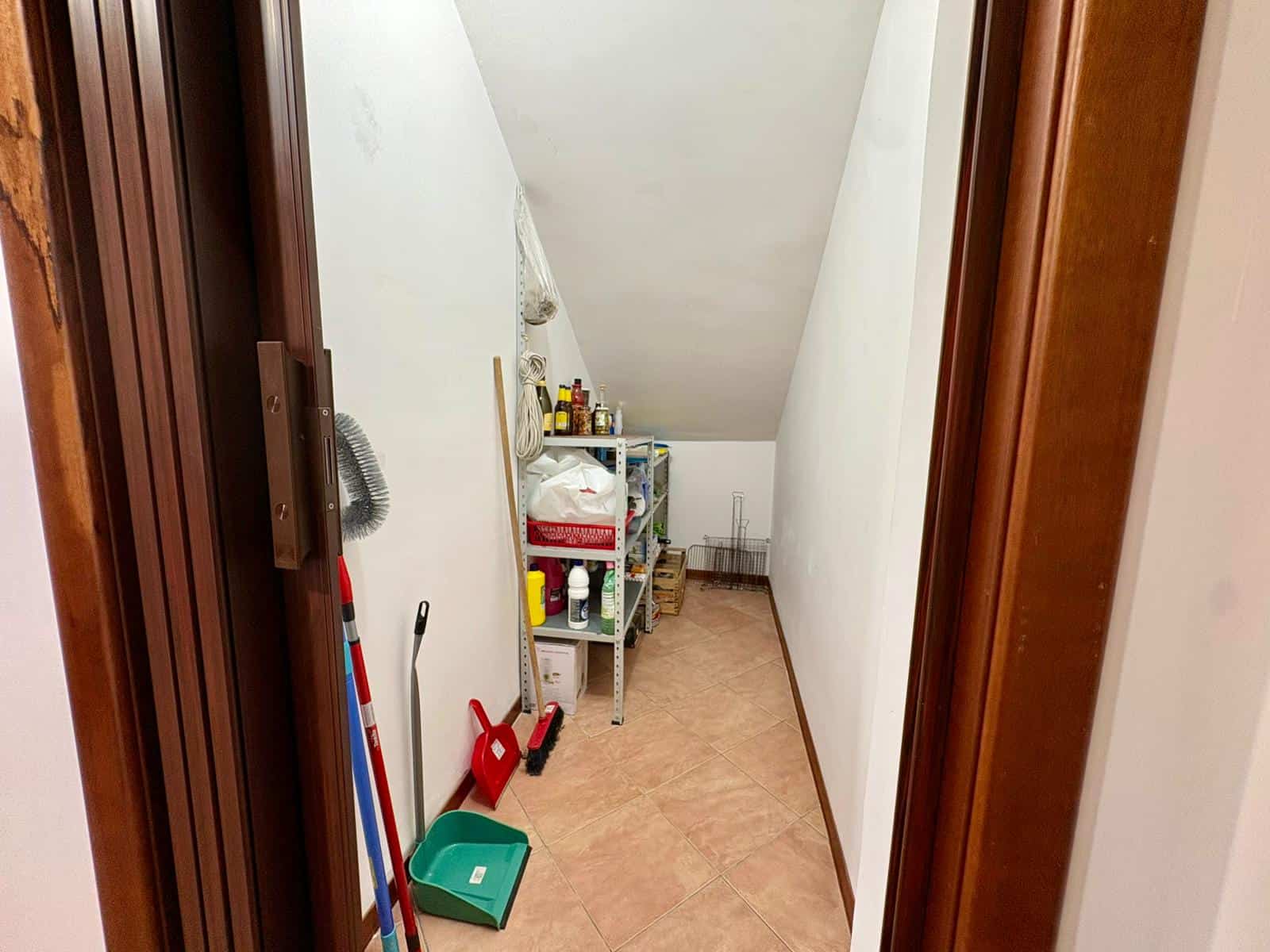 Ripostiglio in soffitta con scaffali e attrezzi per la casa, spazio di stoccaggio funzionale e organizzato, ideale per conservare utensili, prodotti di pulizia e materiali vari in modo ordinato.