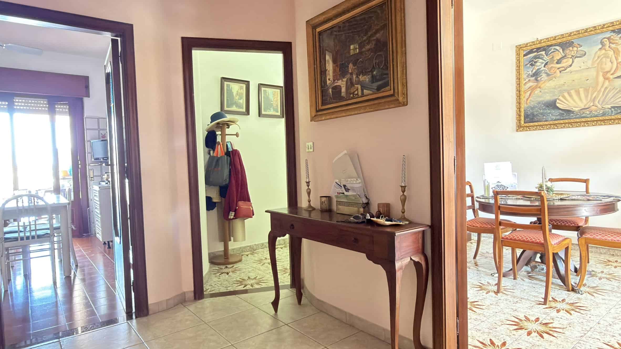 Porte d'ingresso e ingresso di un appartamento con arredamento classico e decorazioni eleganti, vista da un corridoio che collega diverse stanze di una casa spaziosa e luminosa.