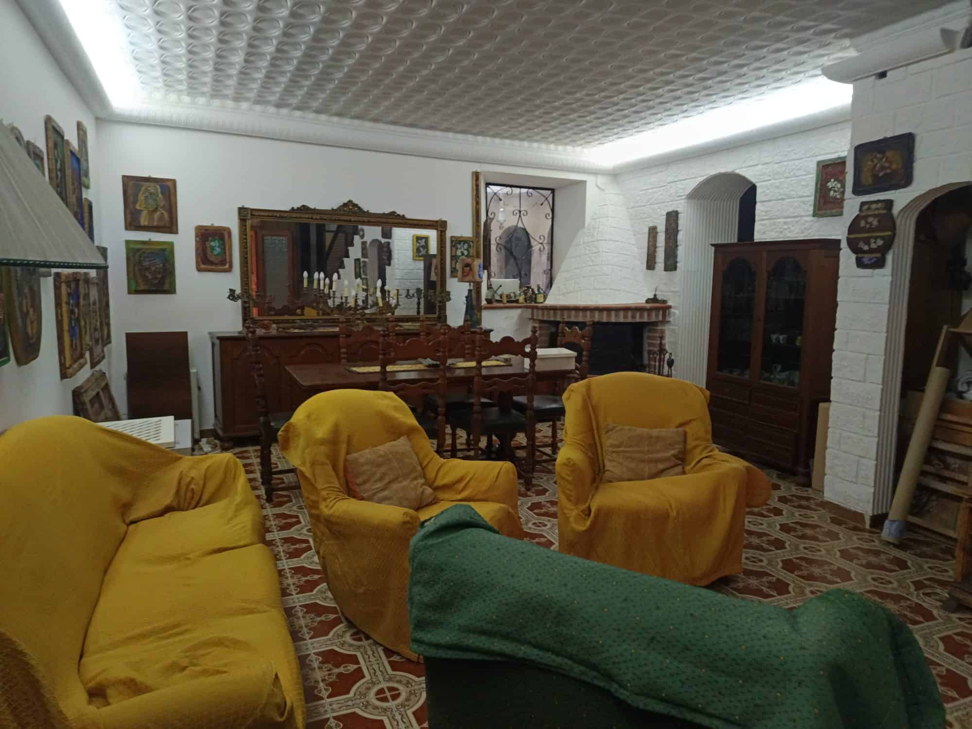 Antistante a un soggiorno accogliente con mobili vintage, sedie e divani con coperture gialle, camino in pietra e pareti decorate con quadri e specchi, ambiente caldo e invitante.