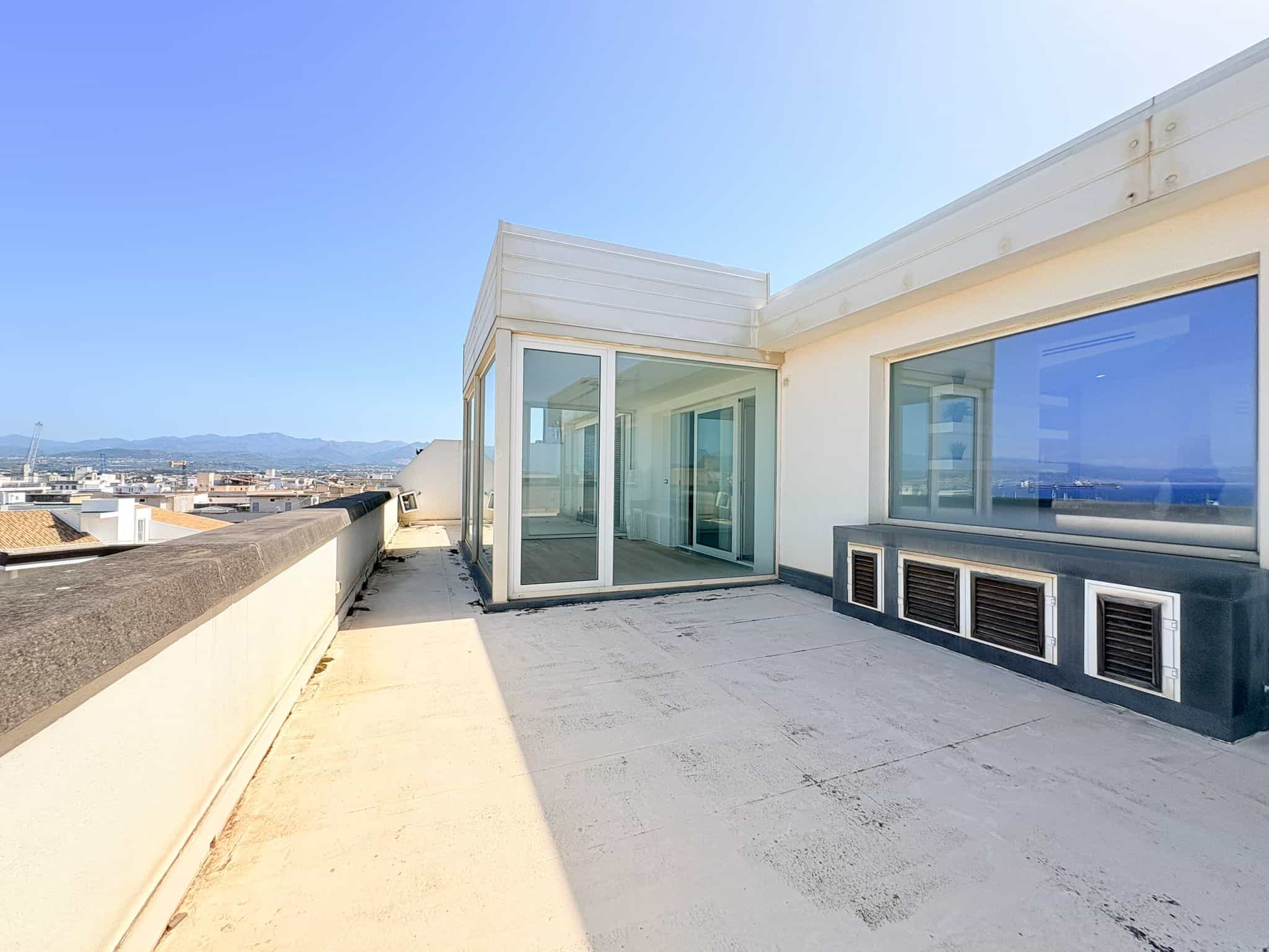 Balcone panoramico di un attico moderno con grandi finestre e vista sulla città e le montagne, ideale per relax e intrattenimento.