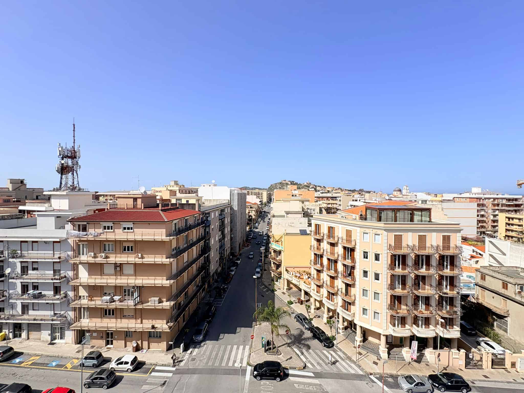 Balcone di un quartiere urbano con edifici residenziali e strada trafficata sotto un cielo sereno.