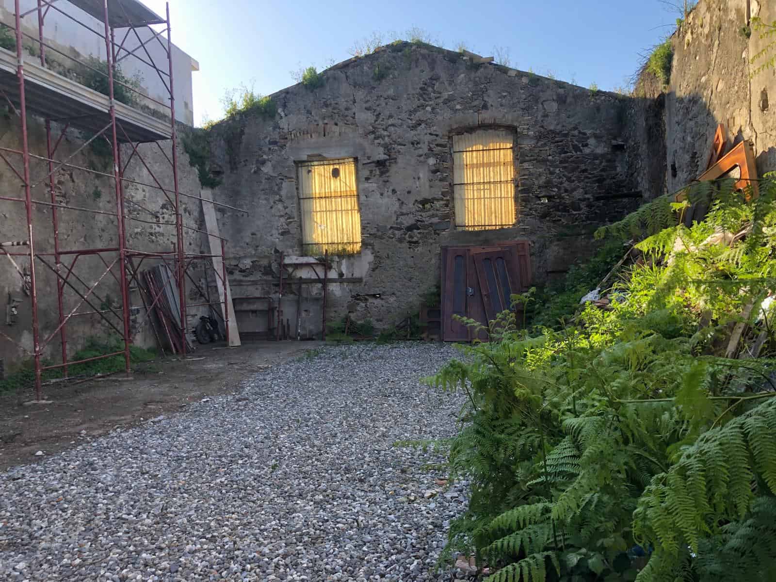 Restauro di un edificio storico con pareti in pietra e finestre in ferro, situato in un'area verdeggiante, ideale per progetti di ristrutturazione e valorizzazione immobiliare in Italia.