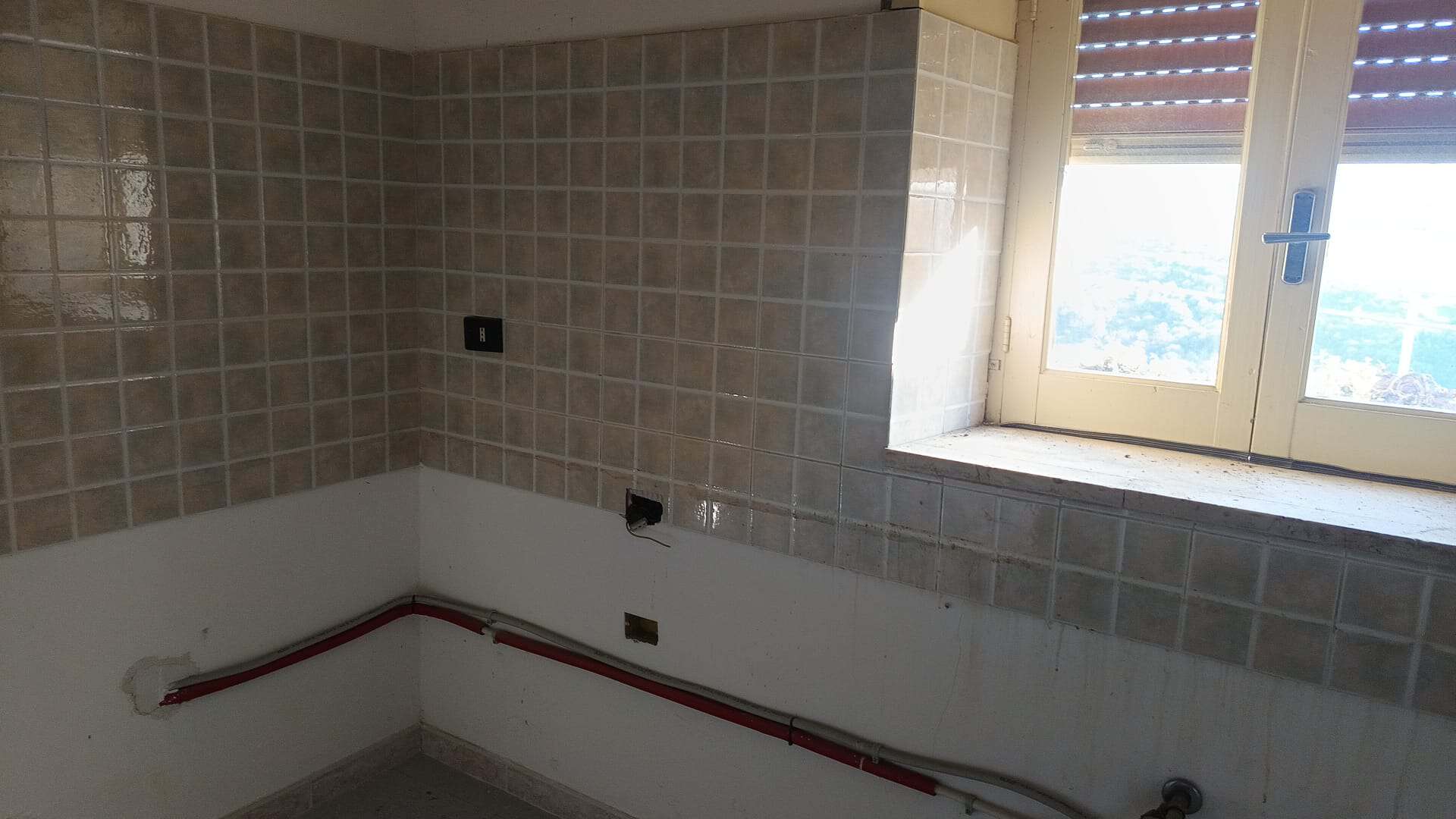 Pannello di parete in piastrelle beige e finestra con vista panoramica, ambiente in fase di ristrutturazione.