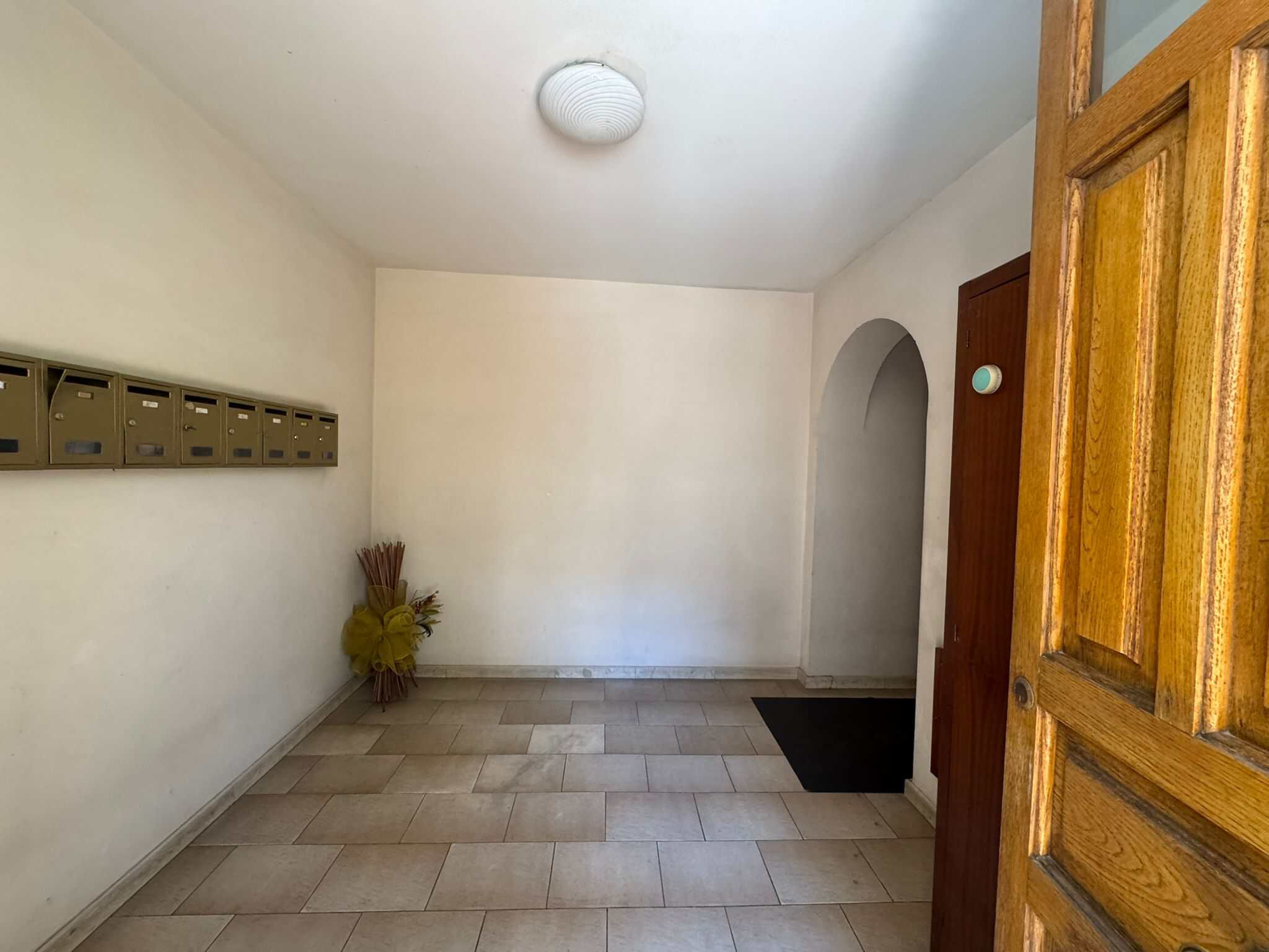 Posto di consegna delle lettere con pareti bianche e pavimento in piastrelle beige, decorato con un mazzo di fiori secchi in un angolo, ingresso di un appartamento o condominio.