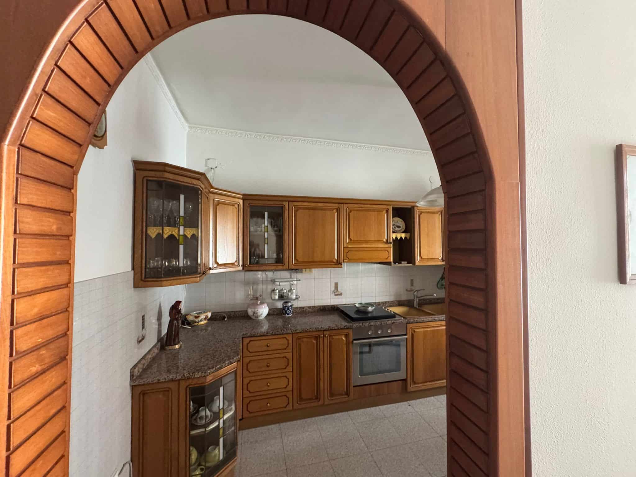 Porte in legno con arco che conduce a una cucina tradizionale con mobili in legno e piano di lavoro in granito, ambiente accogliente e rustico.