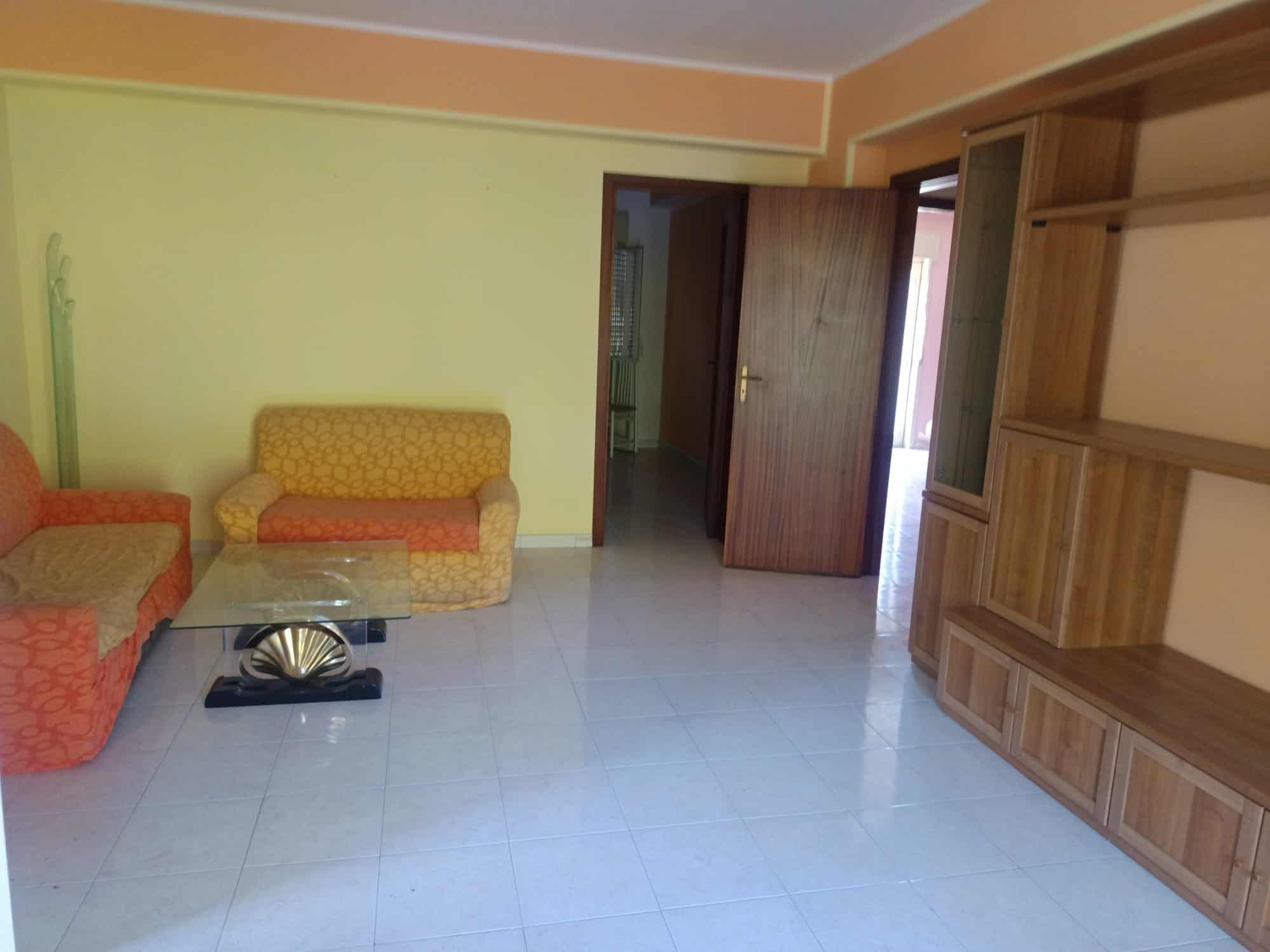 Ampia zona soggiorno con divani colorati e mobile in legno, ideale per affitti turistici o residenziali, con accesso a balcone e ambiente luminoso.