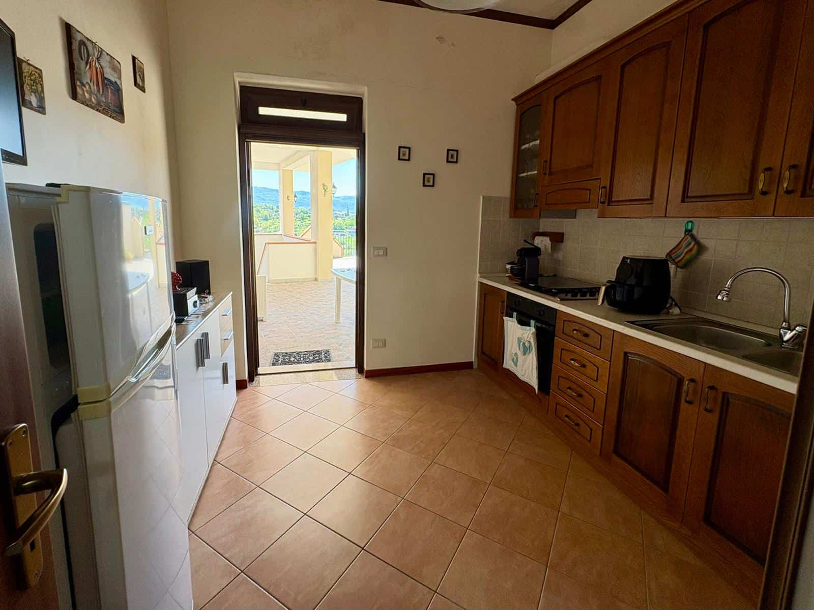 Ampia cucina con mobili in legno, frigorifero, forno e accessori, vista su balcone con paesaggio naturale, ambiente luminoso e accogliente, ideale per soggiorni in famiglia o coppie.