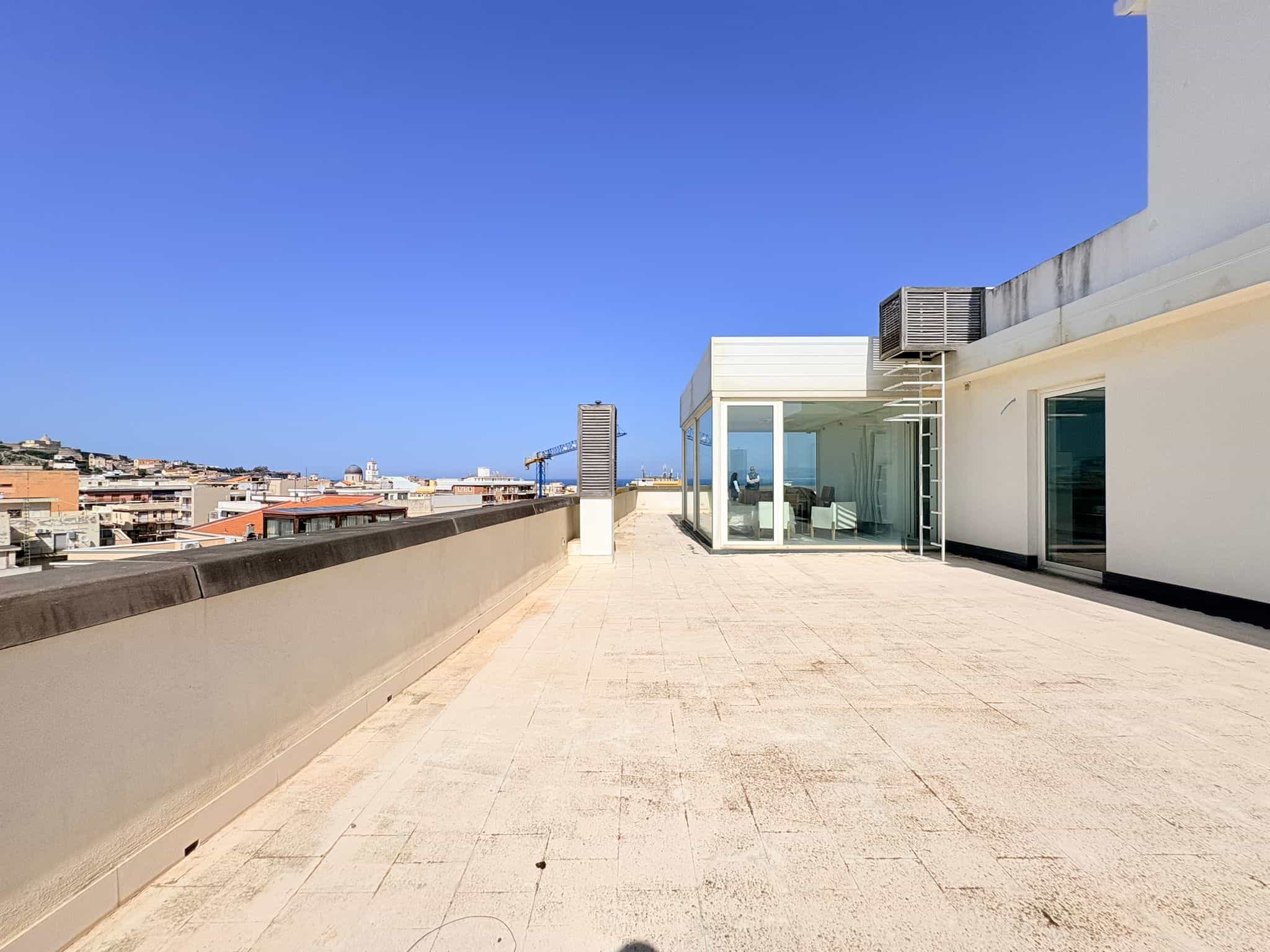 Balcone panoramico di un edificio moderno con vista sulla città e sul mare, spazio esterno con pavimentazione chiara e pareti bianche, ideale per relax e socializzazione all'aperto.