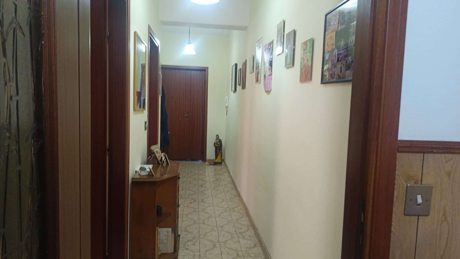 Ampia vista di un corridoio interno di una casa con pareti decorate, pavimento in piastrelle e illuminazione soffusa, ideale per ambienti residenziali accoglienti e ben arredati.