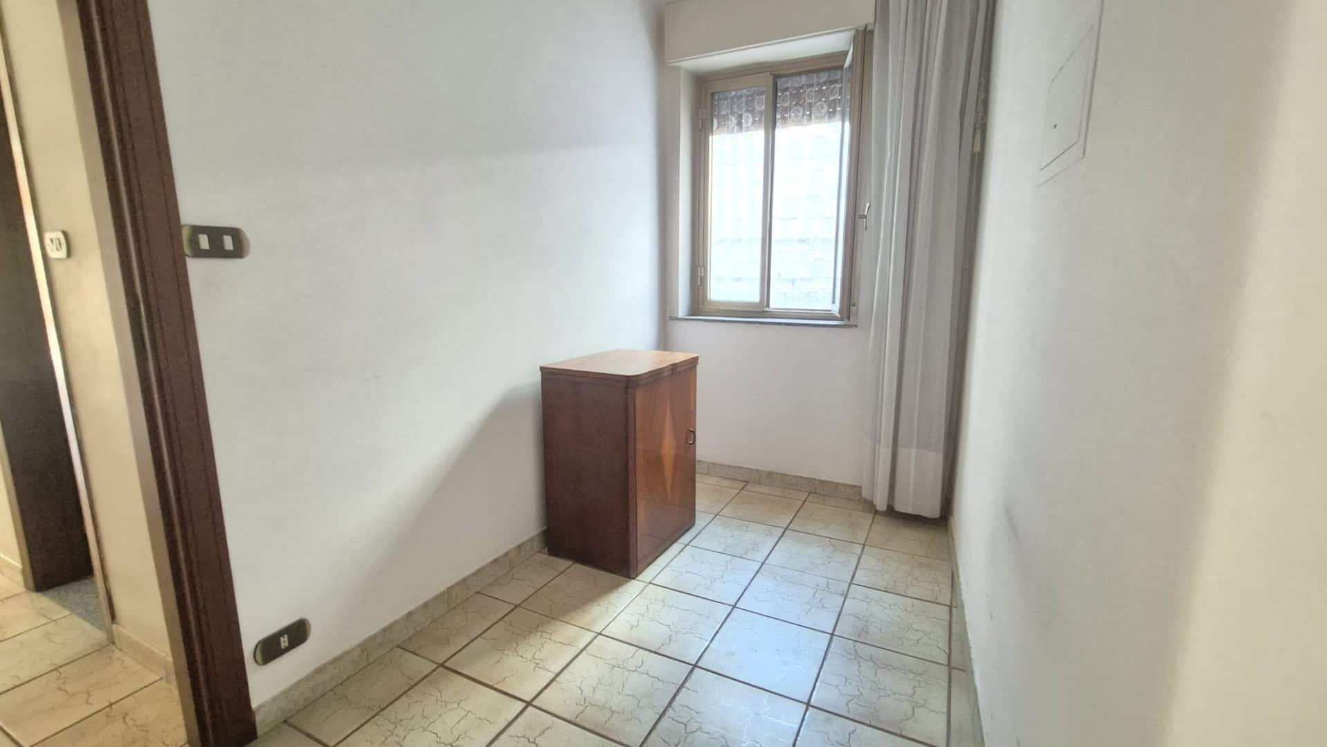 Spazio vuoto in una stanza con pareti bianche, finestra e pavimento in piastrelle, ideale per ristrutturazione o arredamento personalizzato.
