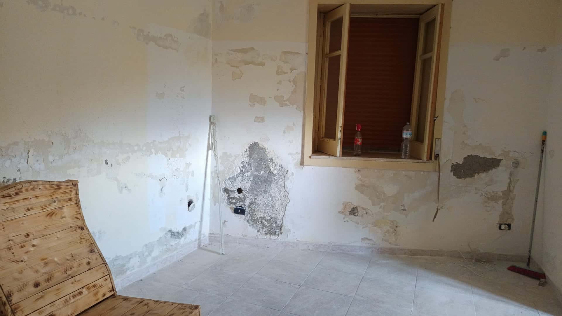 Pannello di parete in fase di ristrutturazione con pareti danneggiate e finestra aperta, pronto per lavori di restauro e miglioramento edilizio.